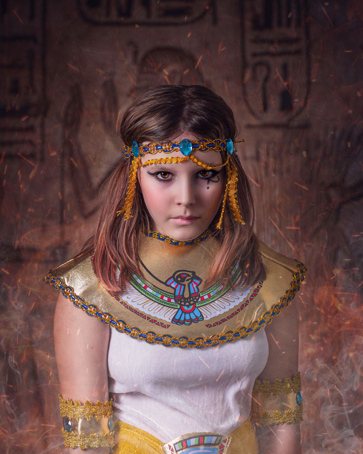 Cosplay portrait featuring Egyptian-inspired gold and turquoise jewelry and headdress against a textured brick wall.
