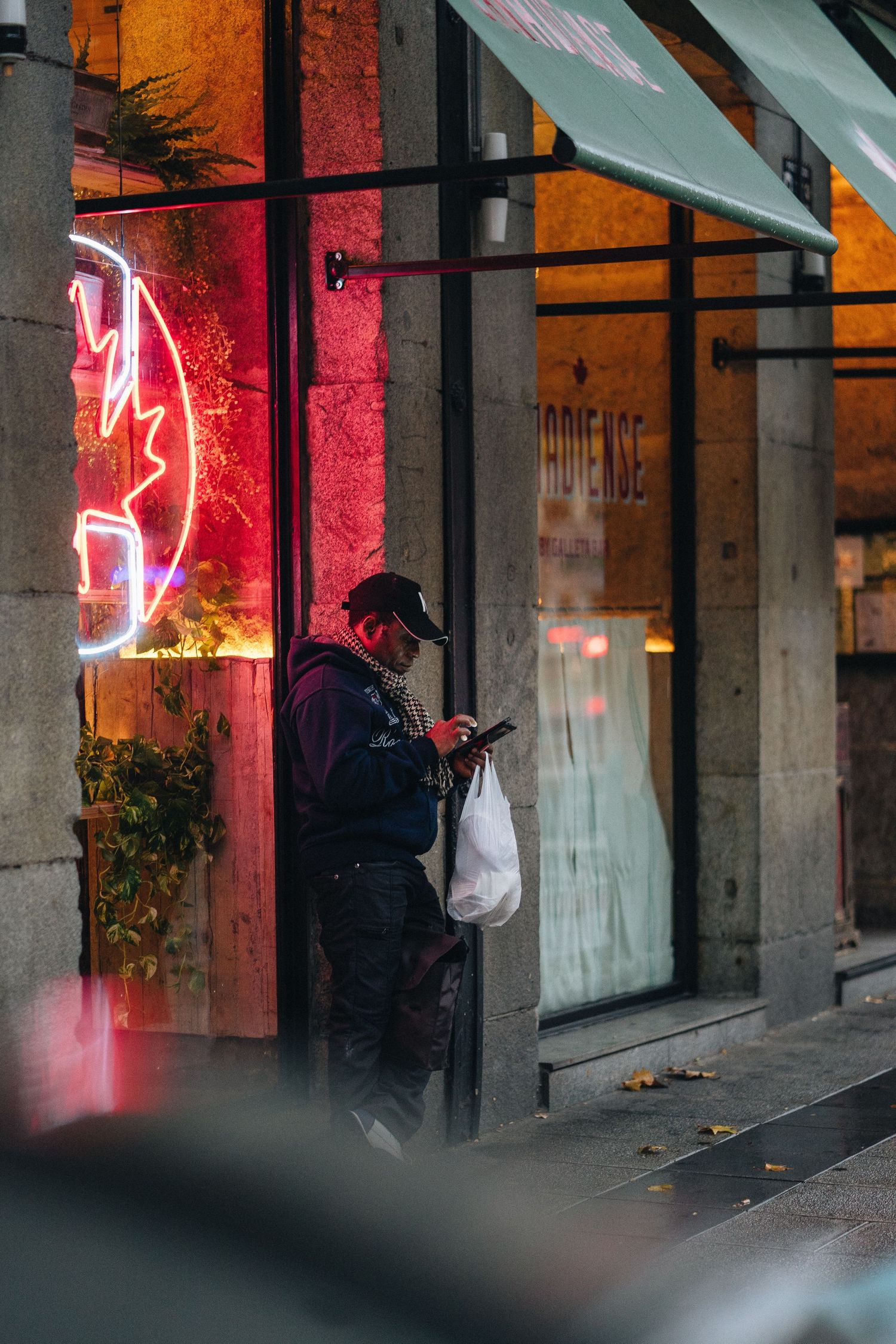 A silhouetted figure checks their phone against a storefront with glowing red neon signage at night.