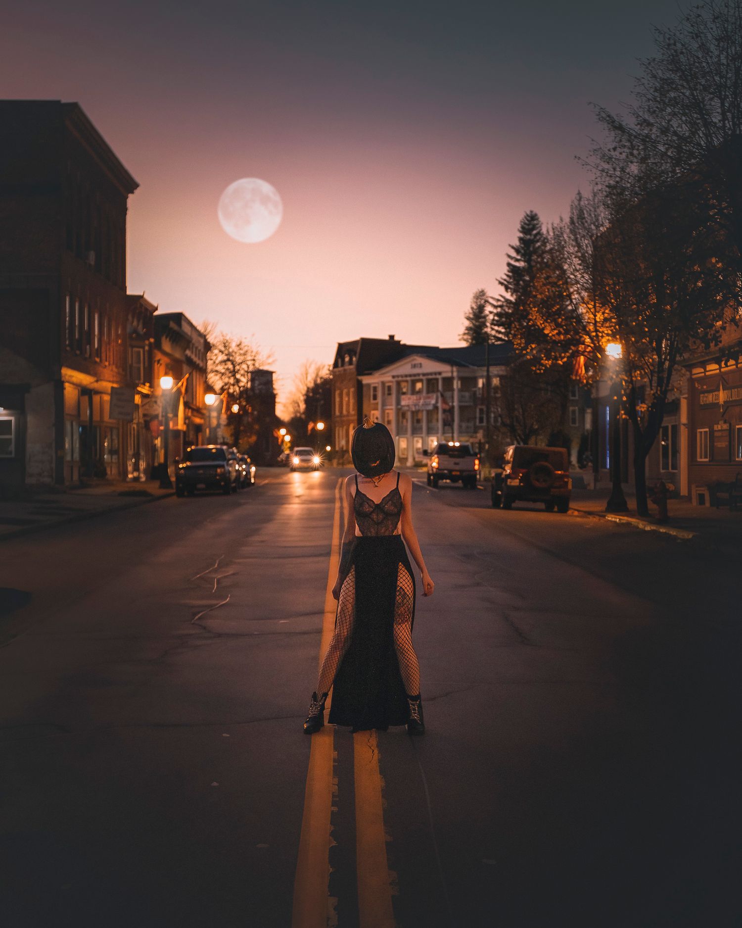 Silhouette standing in empty street at dusk with full moon visible.