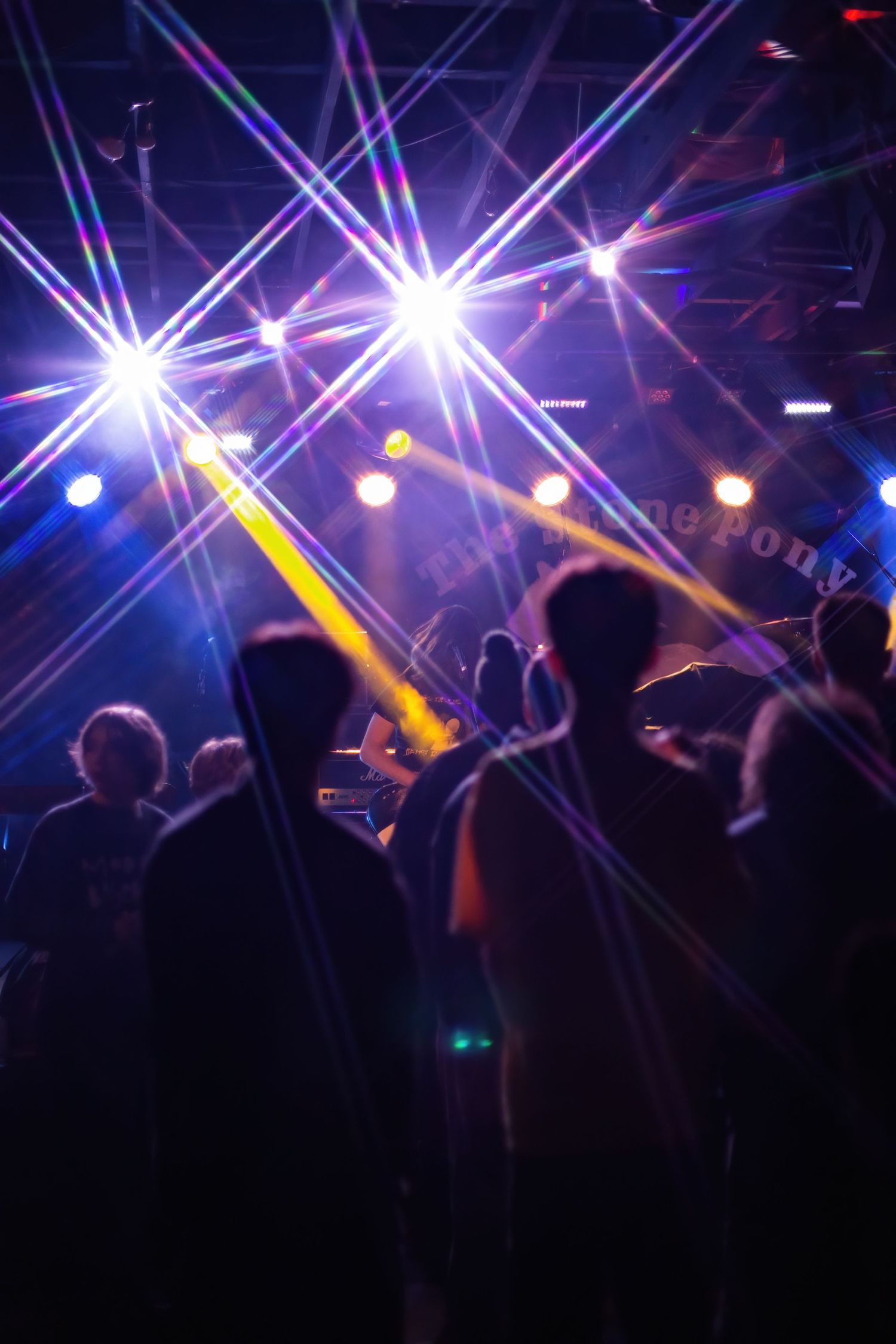 Silhouettes of people dancing under vibrant colorful stage lights with star burst effects at a nightclub event.