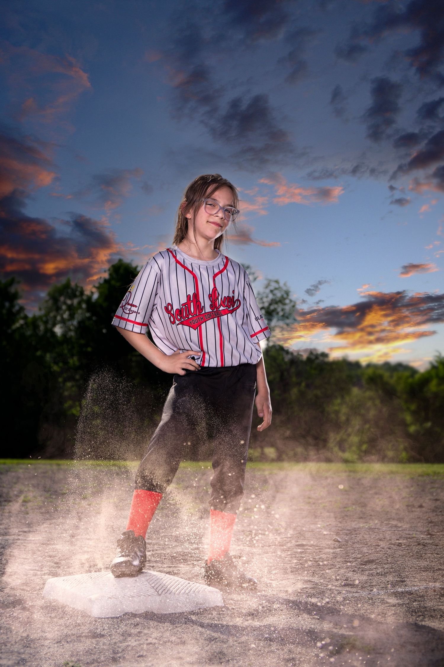 Baseball player kicking up dirt on field during dramatic sunset photoshoot.