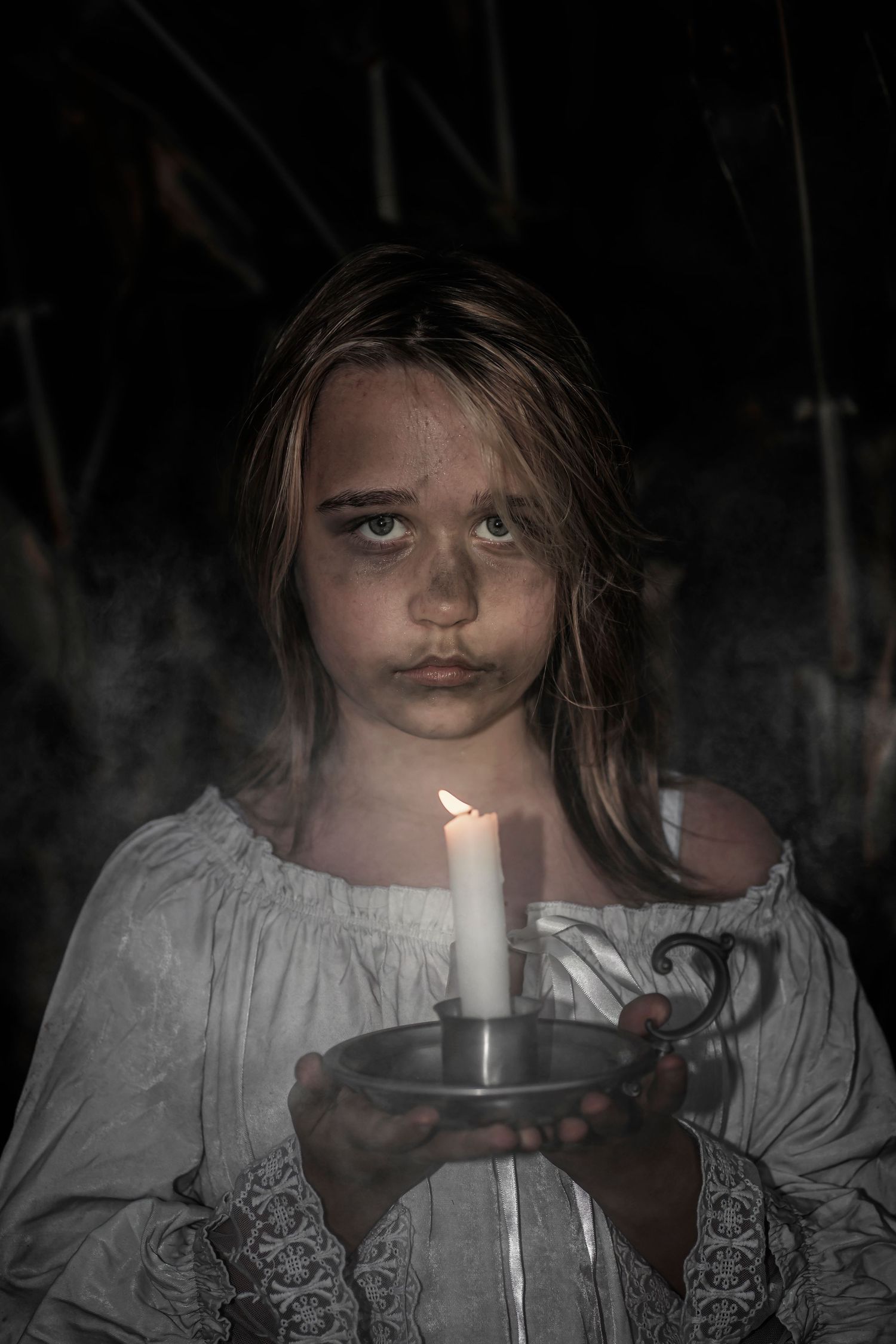 A haunting portrait features a person holding a lit candle in darkness.