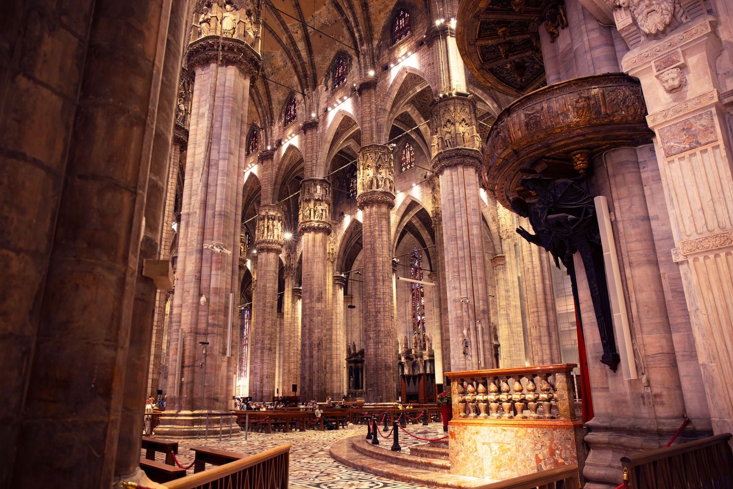Gothic cathedral interior with ornate stone columns, arches, and vaulted ceilings illuminated by warm lighting.
