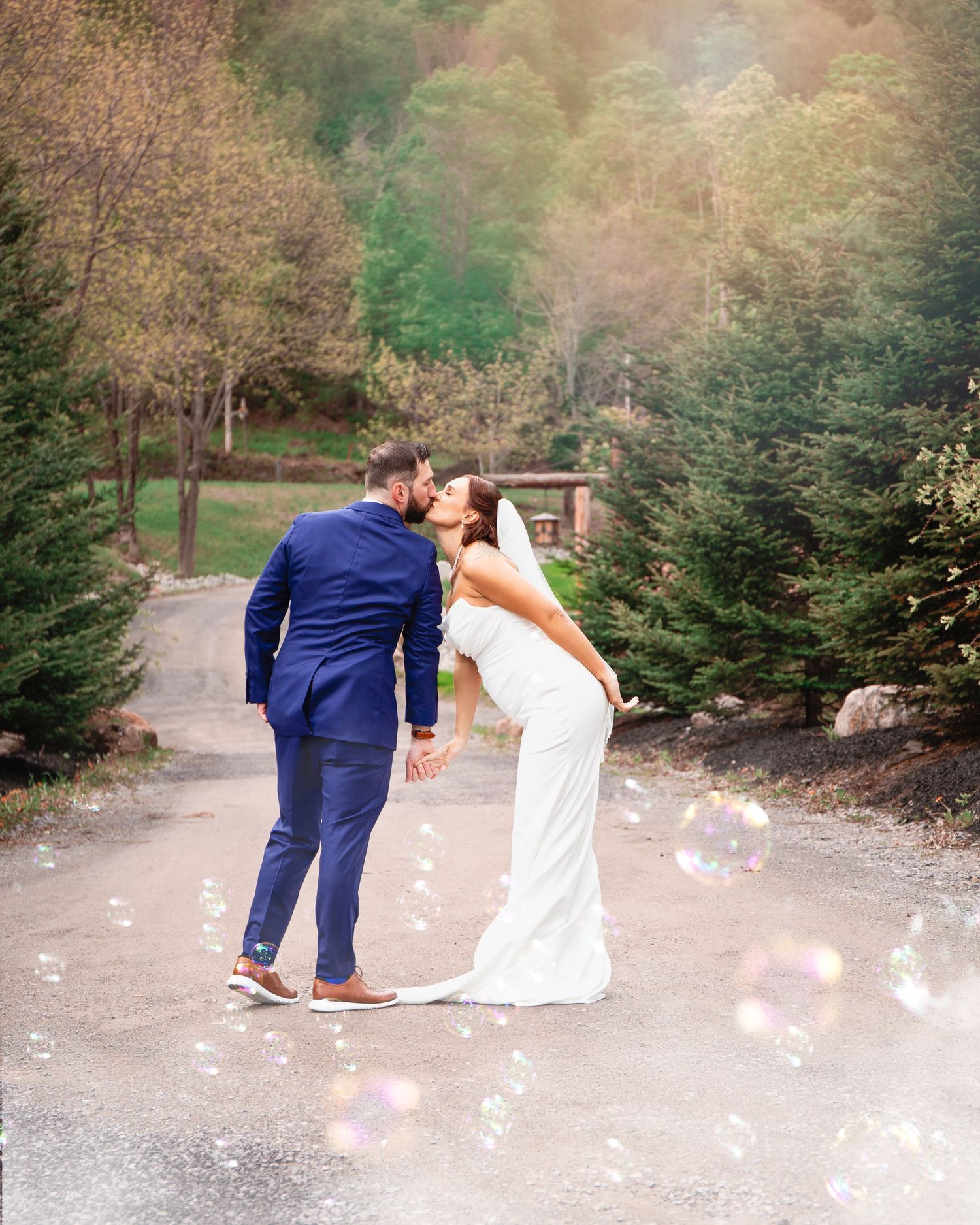 Wedding couple dipping pose with floating bokeh effects on forest path.