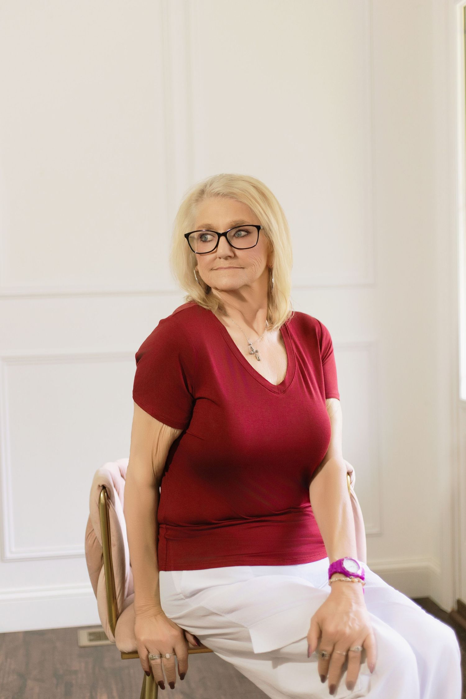 A person in a burgundy top sits in a chair against a white wall.