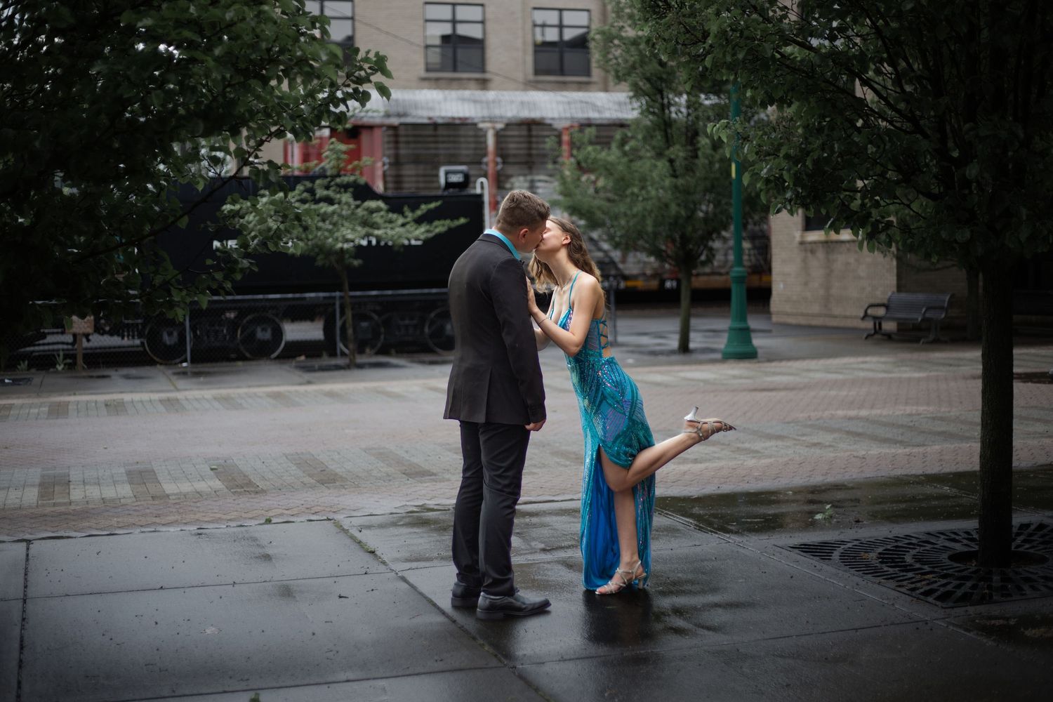 Romantic couple poses together in an urban setting with trees and buildings in background.