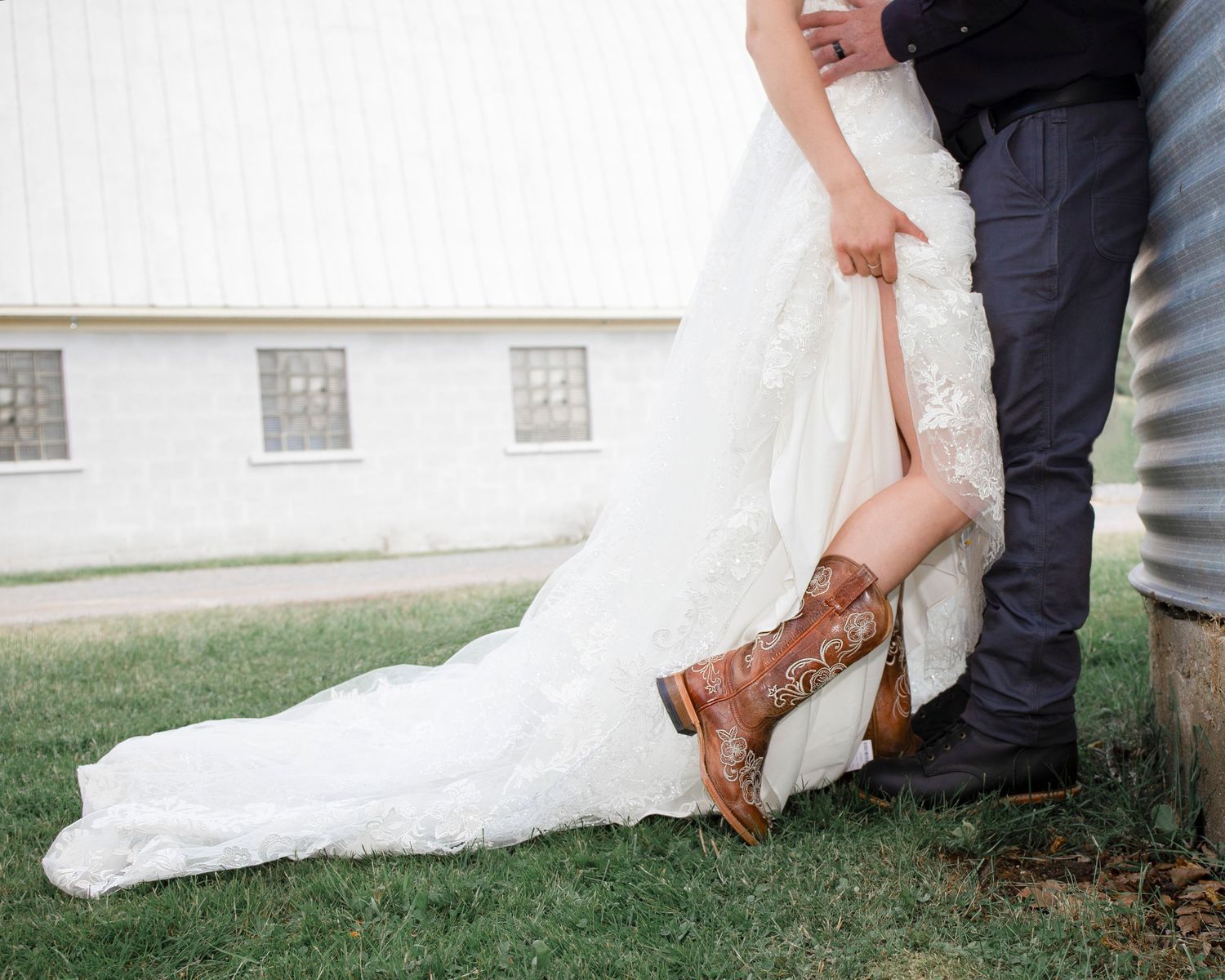 Detail shot of wedding dress train and boots on green grass.