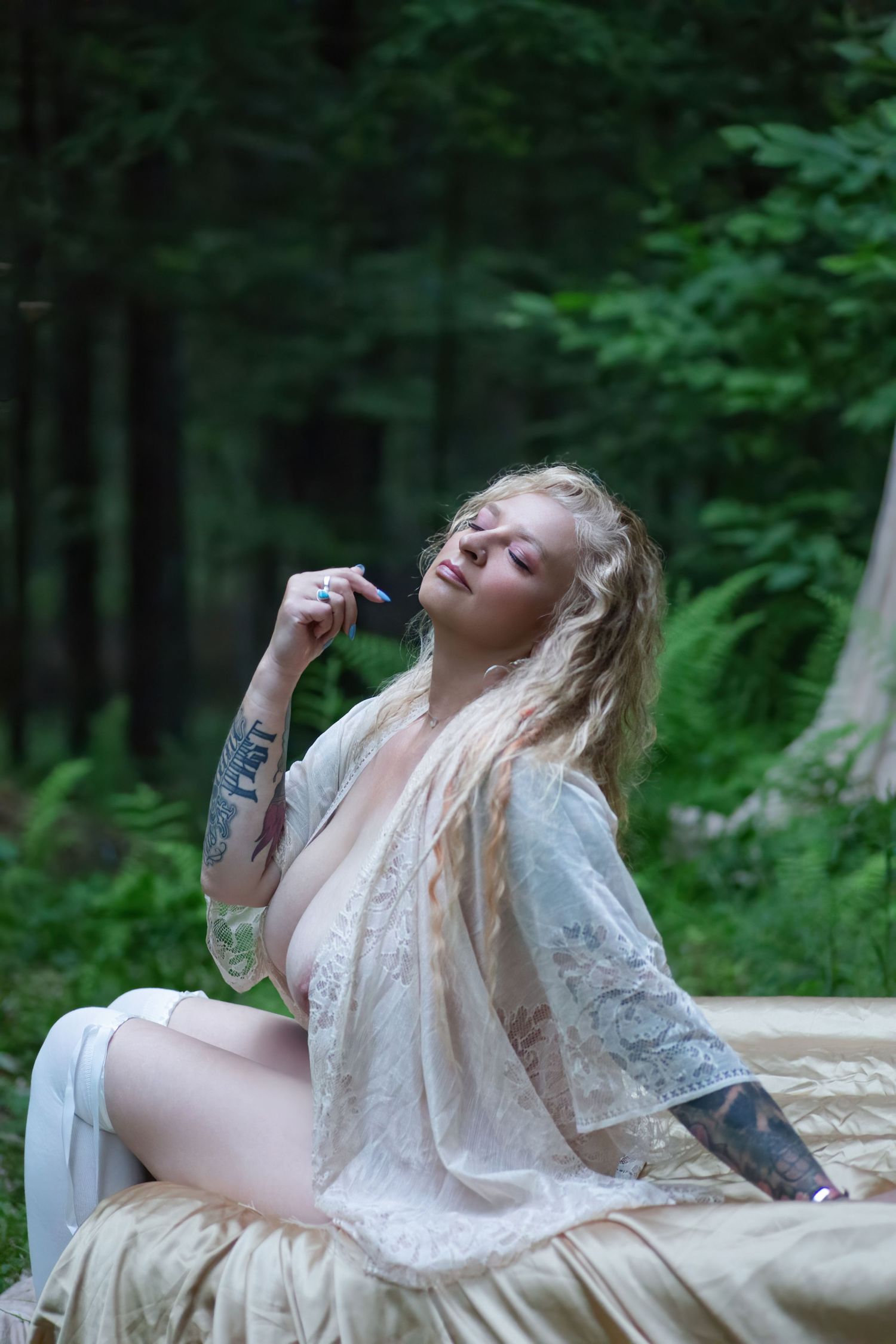A person wearing a white lace garment leans back dramatically on an antique couch in a wooded outdoor setting.