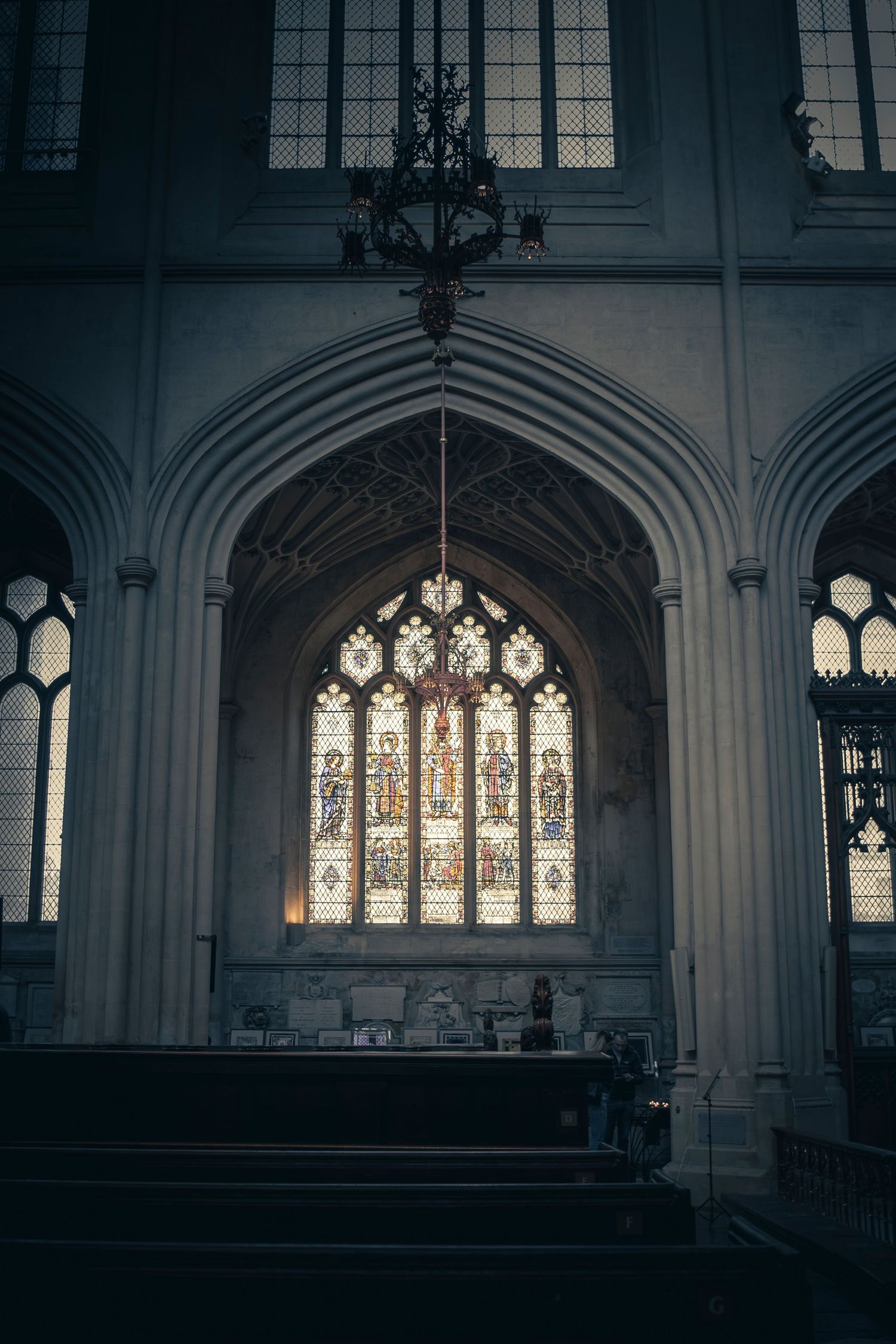 Gothic church interior with arched stained glass windows and ornate architectural details in dramatic lighting.
