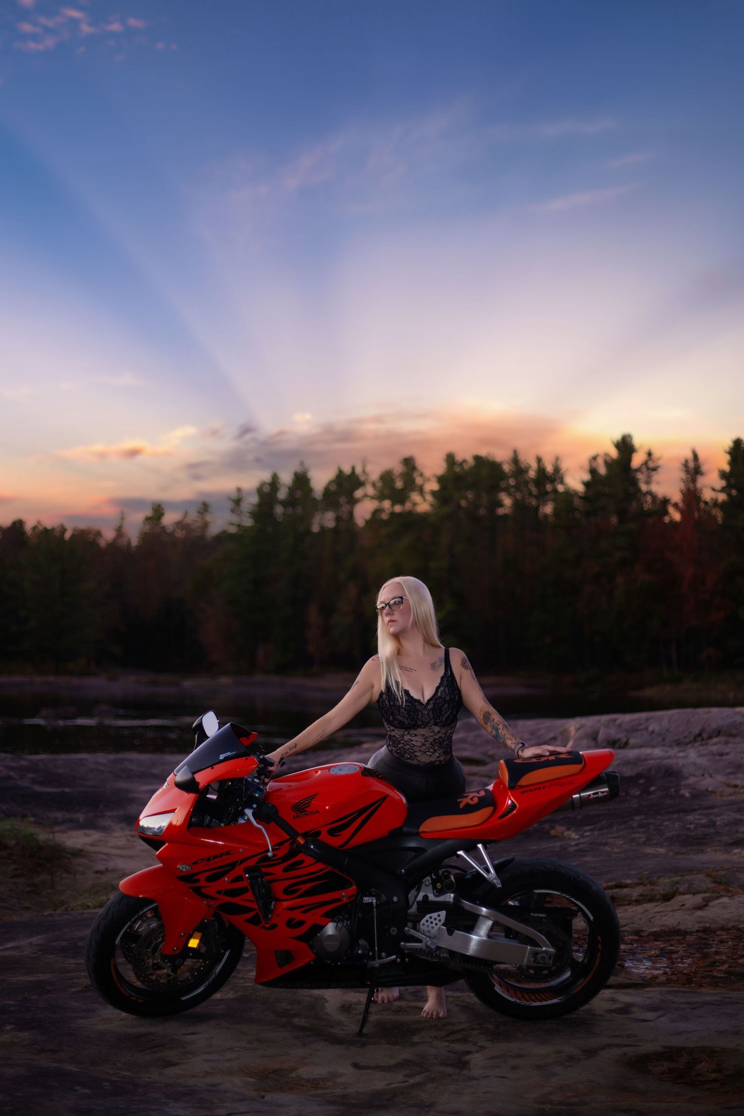 Red sports motorcycle parked at sunset with dramatic sky and forest silhouette in background.