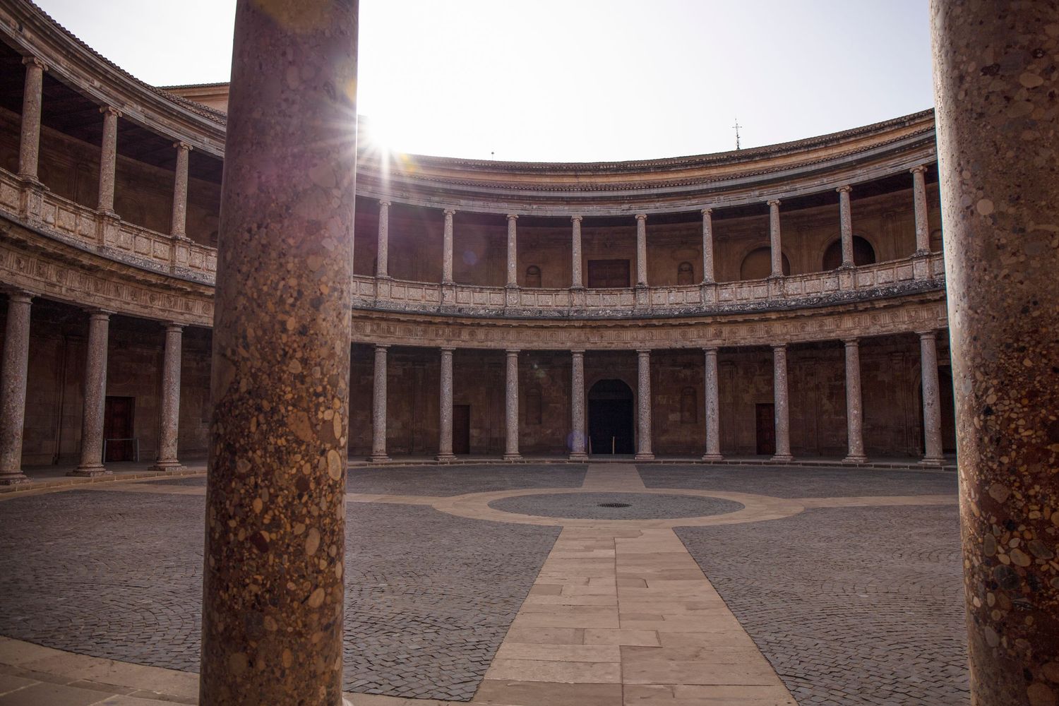 Panoramic view of the historic Palace of Charles V courtyard with circular colonnade and sunlight in Granada, Spain.