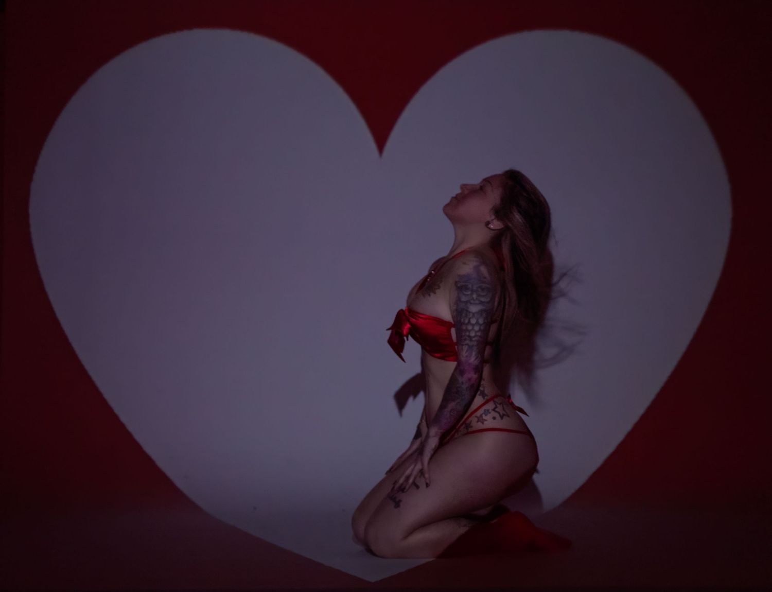 Boudoir photography with heart-shaped lighting effect and red accent lighting.