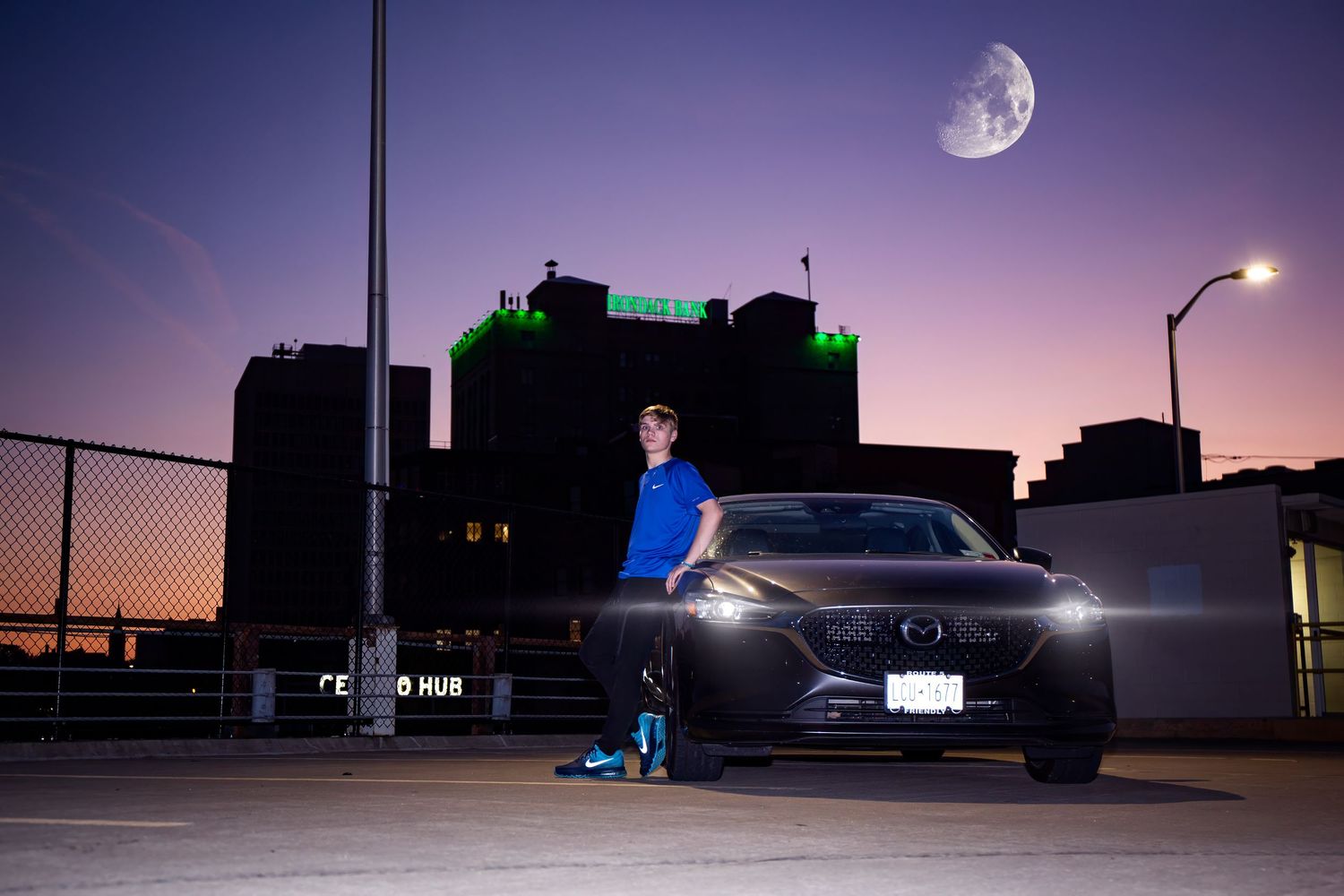 A black sports car parked at night with a large moon in the sky and city buildings silhouetted in the background.