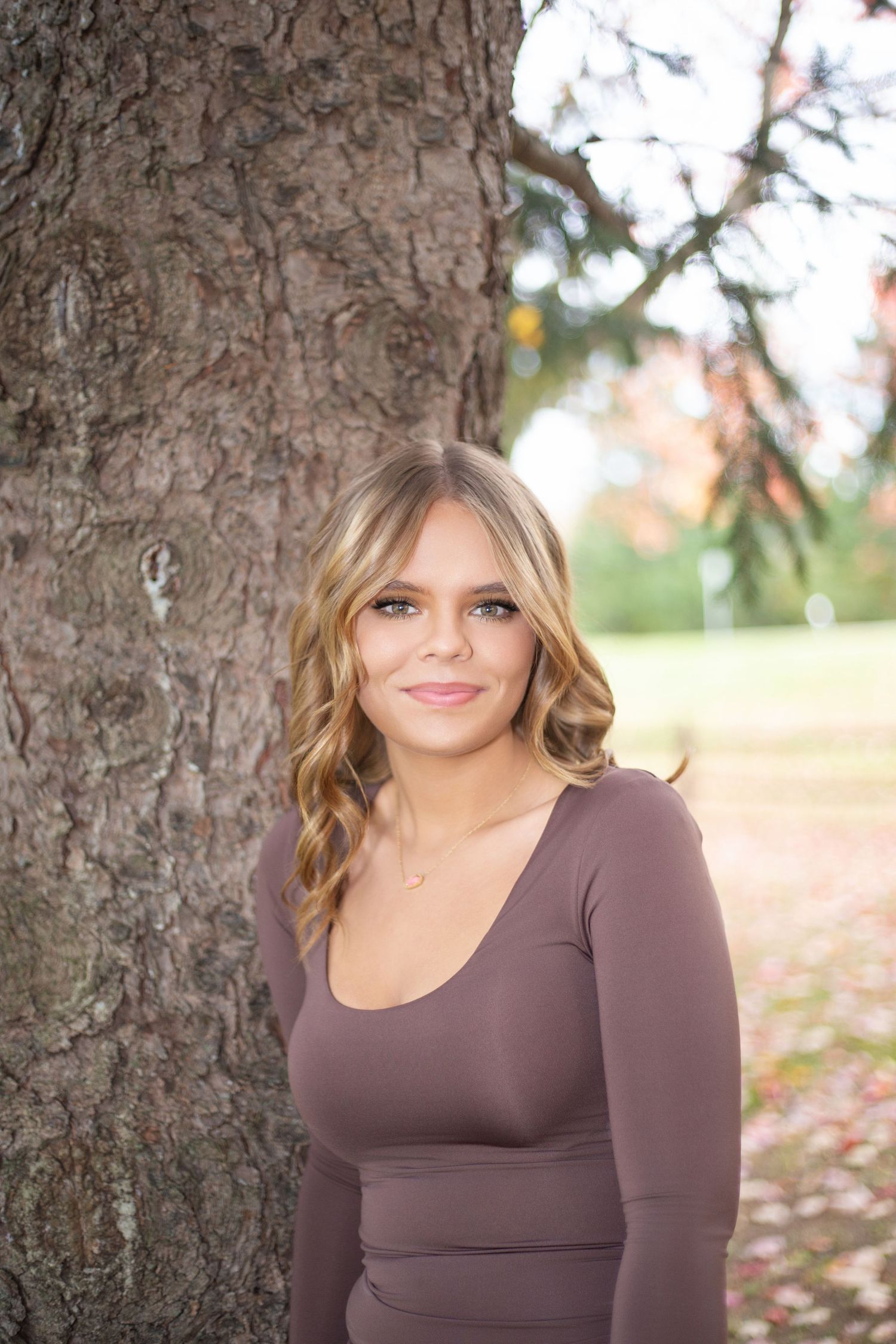 Outdoor portrait against tree trunk showing warm autumn tones and natural lighting.