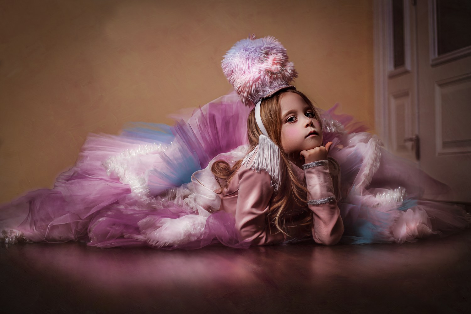 A young girl in a pink tutu dress and floral headpiece sits dreamily on a wooden floor near a white door.