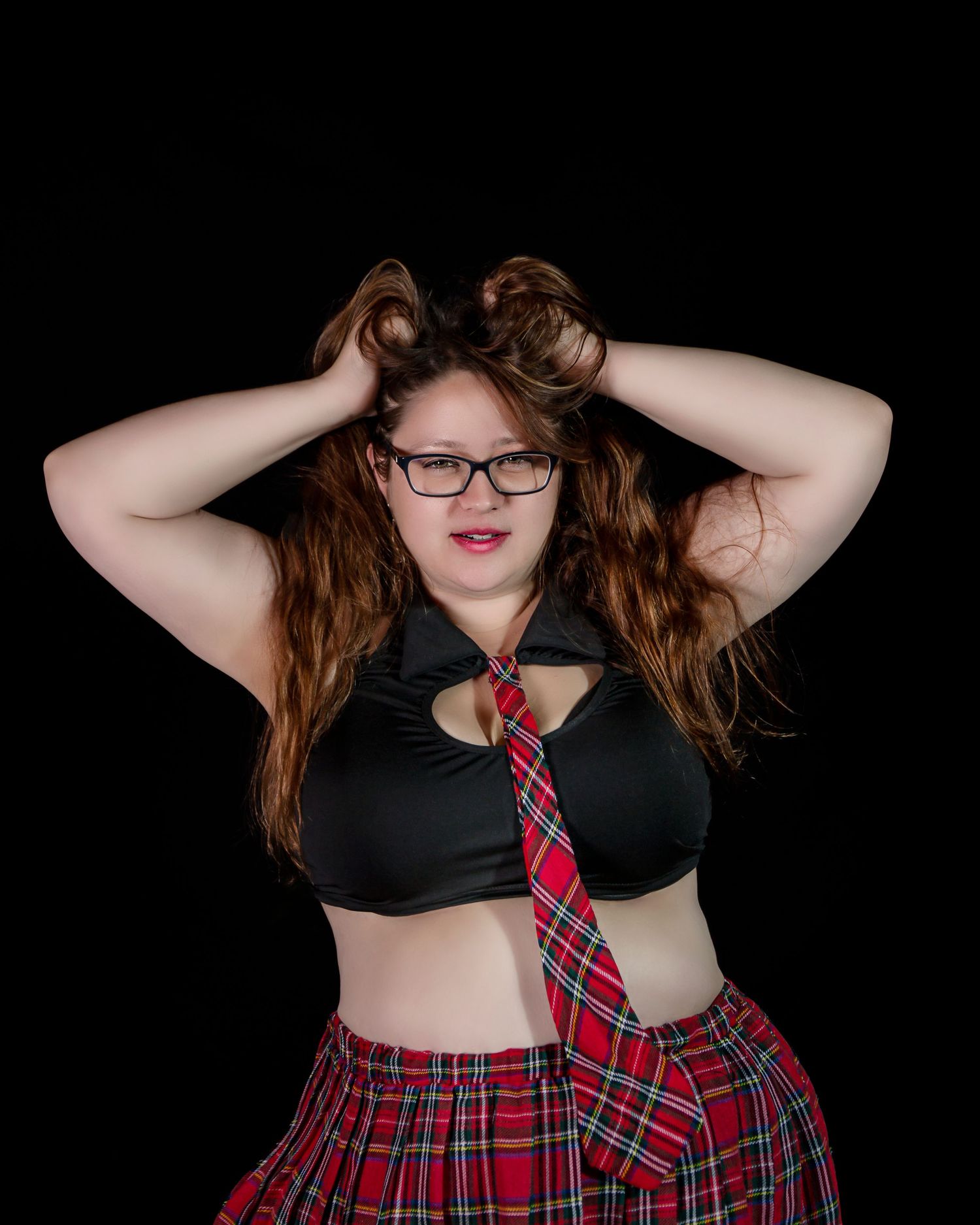 Playful boudoir portrait with plaid skirt and tie against black background.