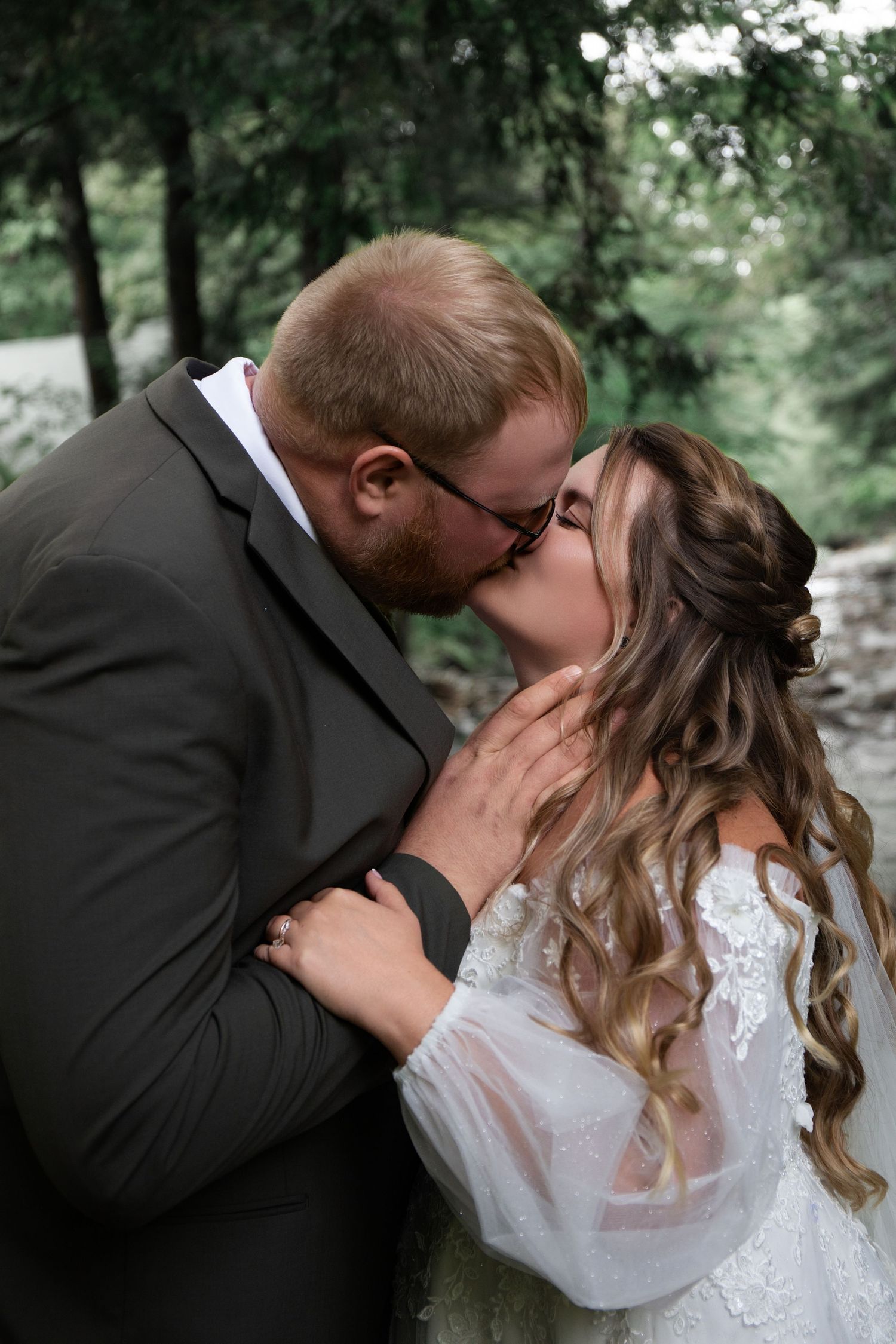 Tender wedding moment captured in natural forest setting with bokeh background.