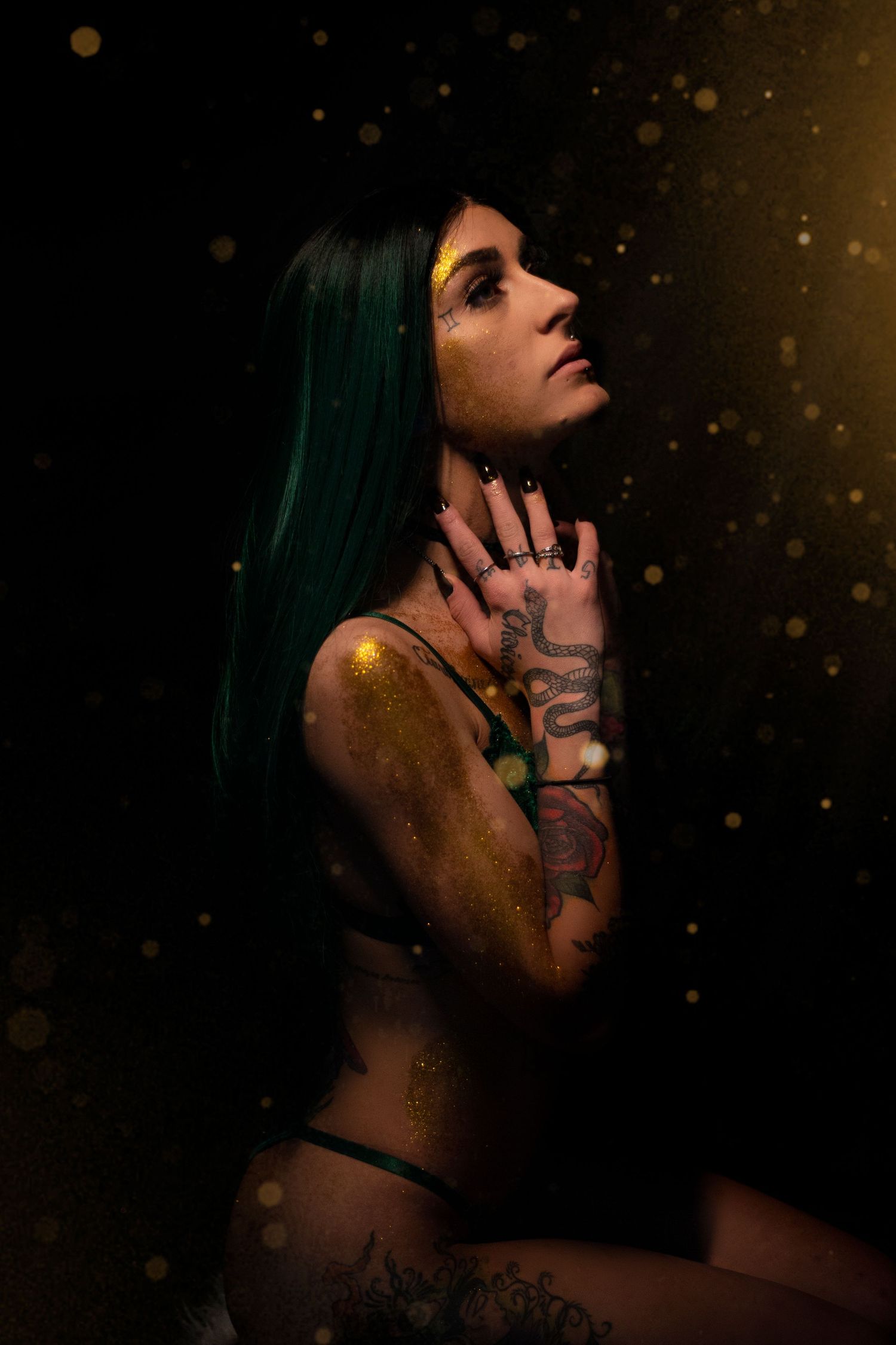 Artistic portrait of a person with green hair in a dark moody setting with glowing particles and tattoos.