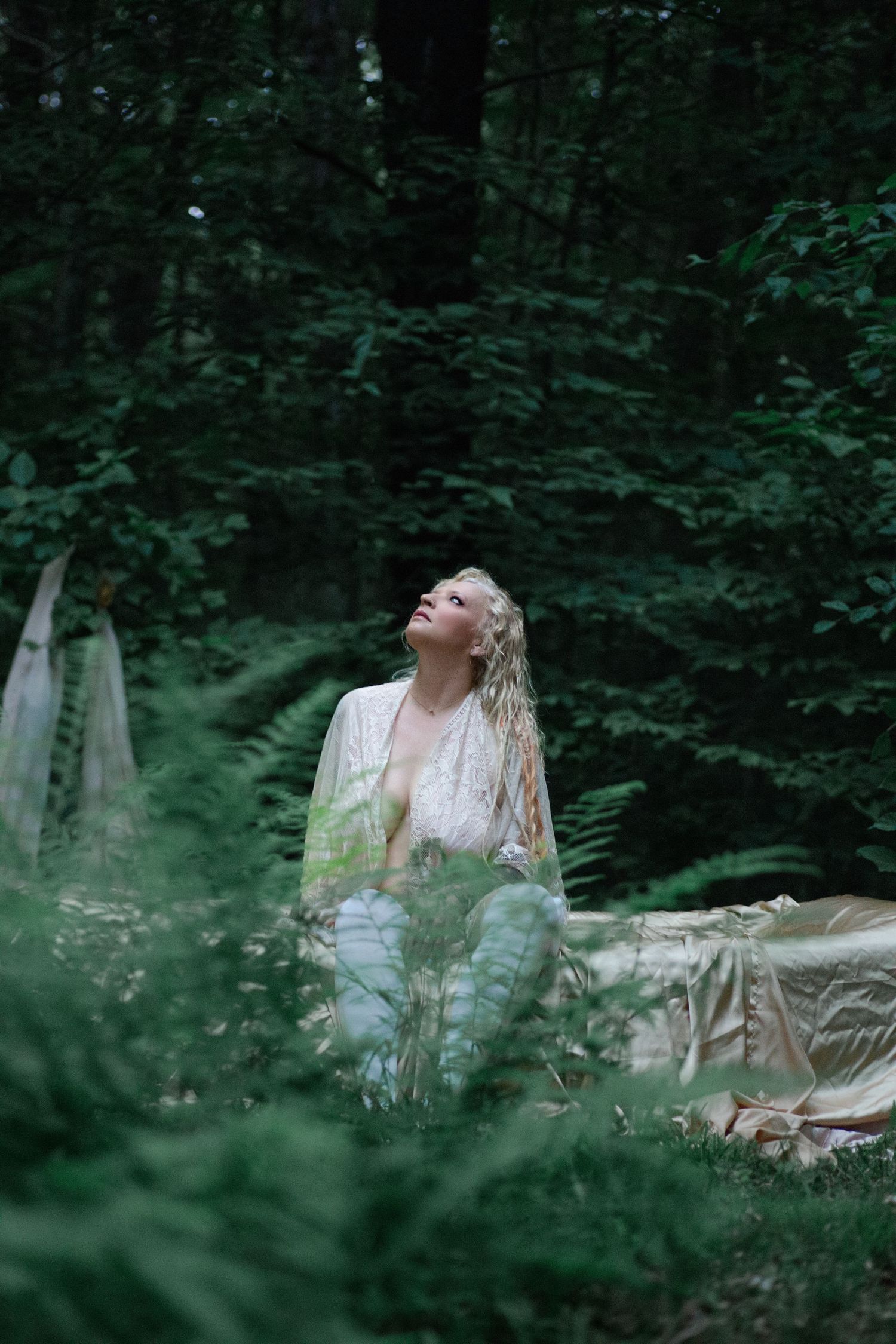 A dreamy forest scene with a figure in white reclining among lush green foliage and dappled sunlight.