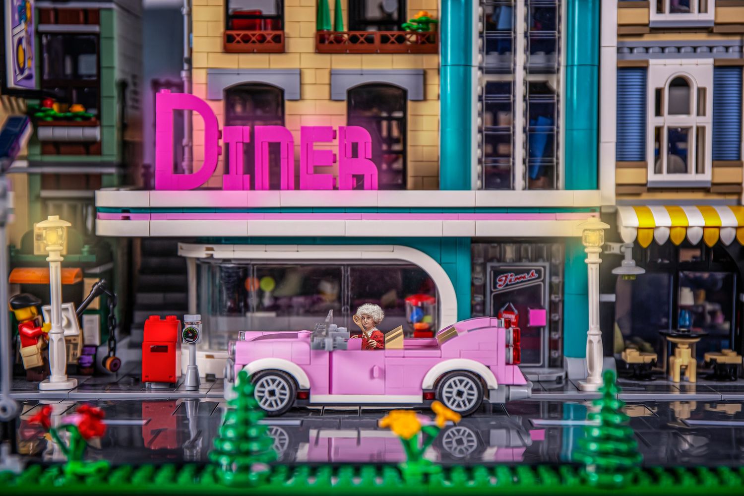 Colorful miniature toy city street scene with vintage cars and buildings in vibrant pink and blue tones.