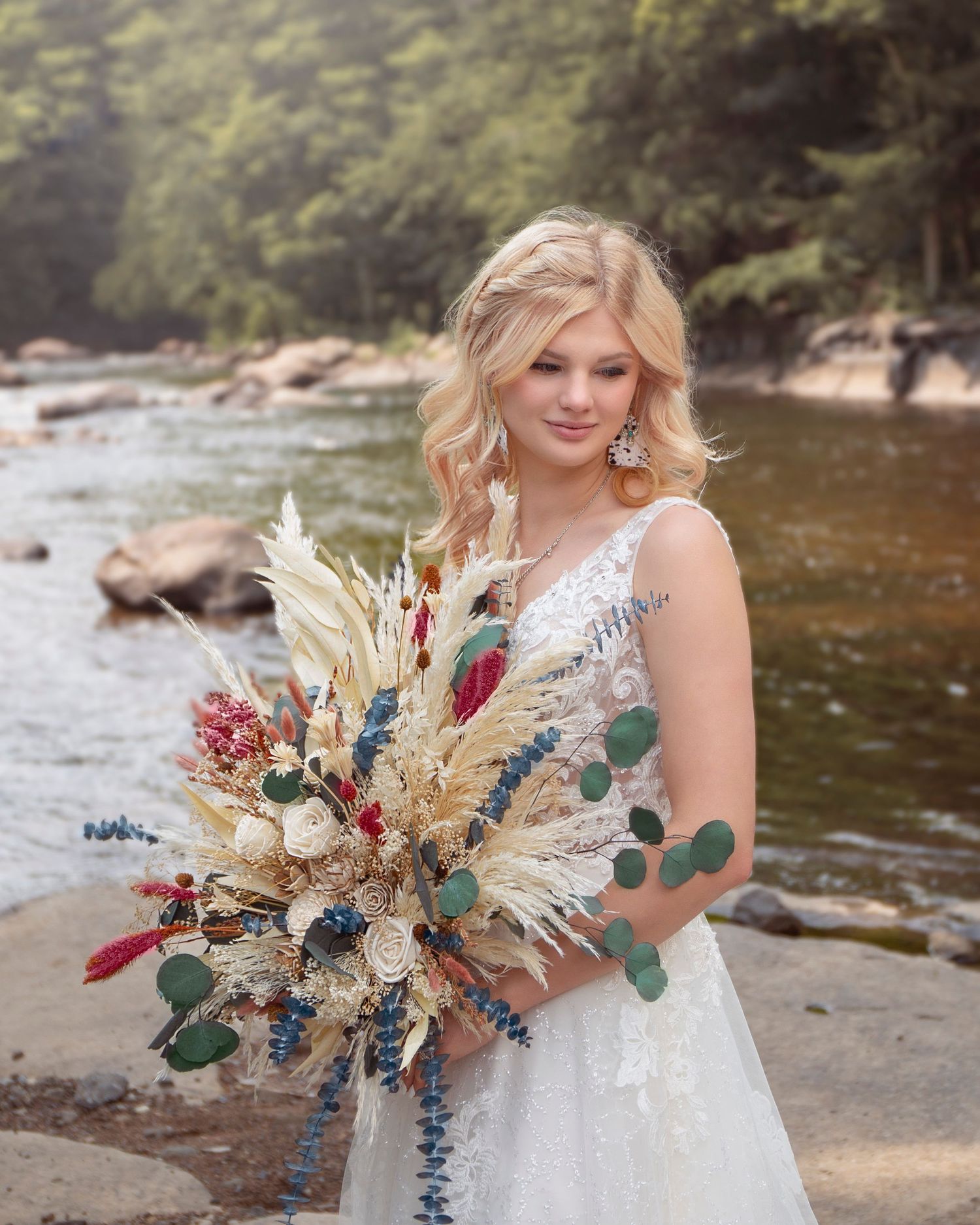 Dried flower wedding bouquet with blue and burgundy blooms against natural river backdrop.