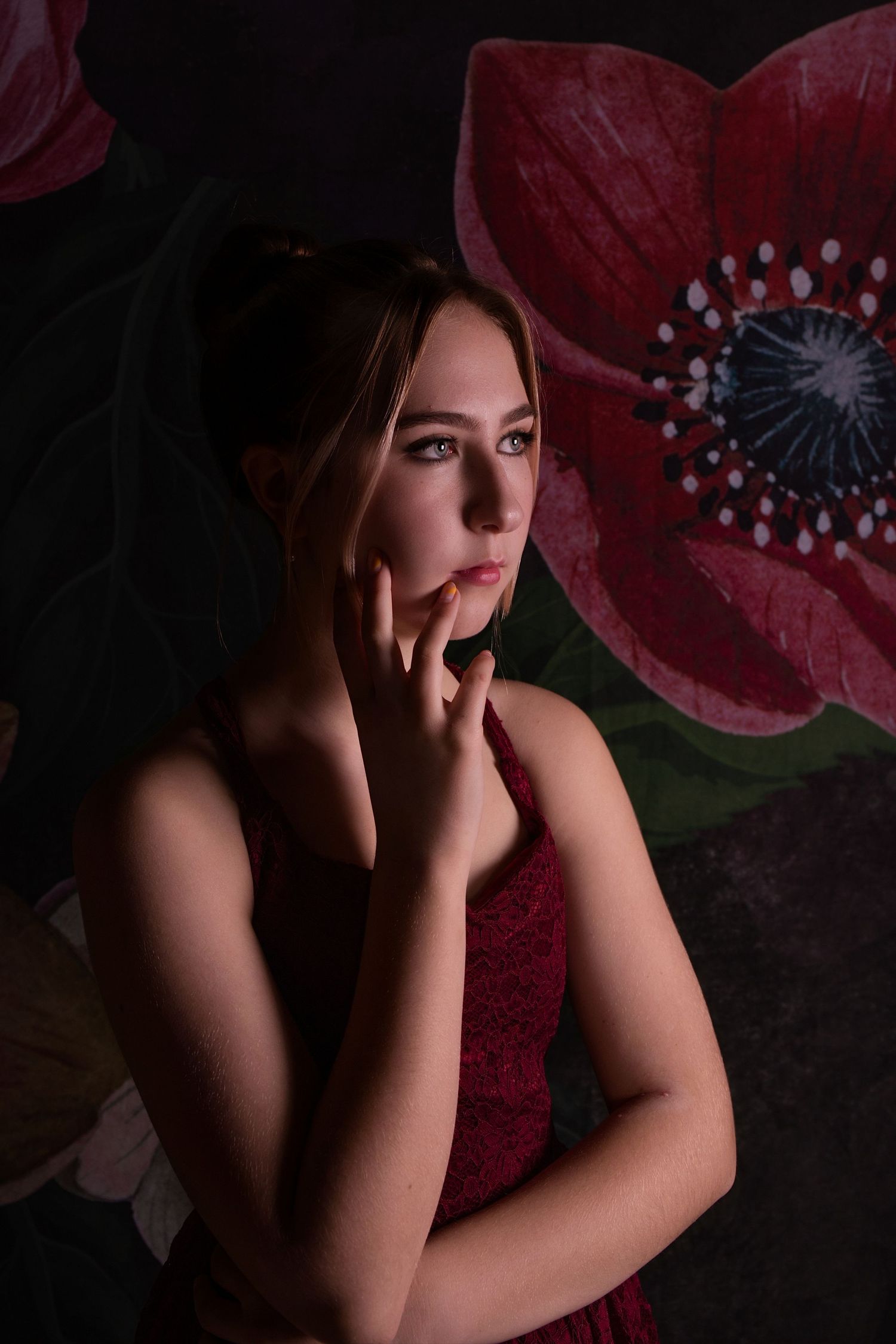Artistic portrait against dark floral backdrop with red poppies in dramatic lighting.