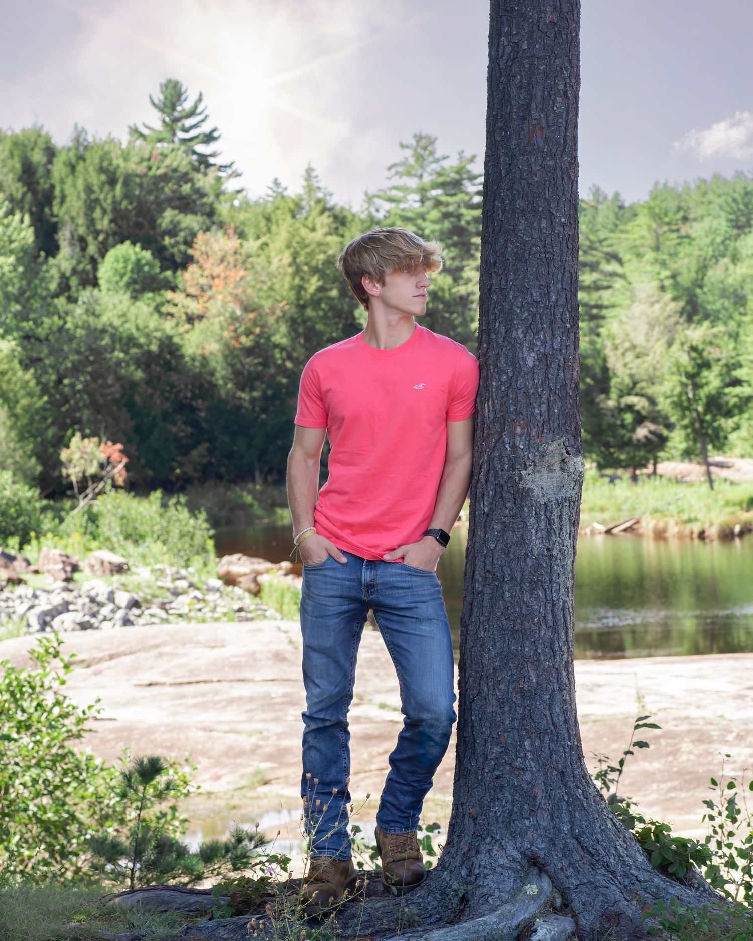 Casual portrait of someone in a bright red t-shirt leaning against a tree by a lake.