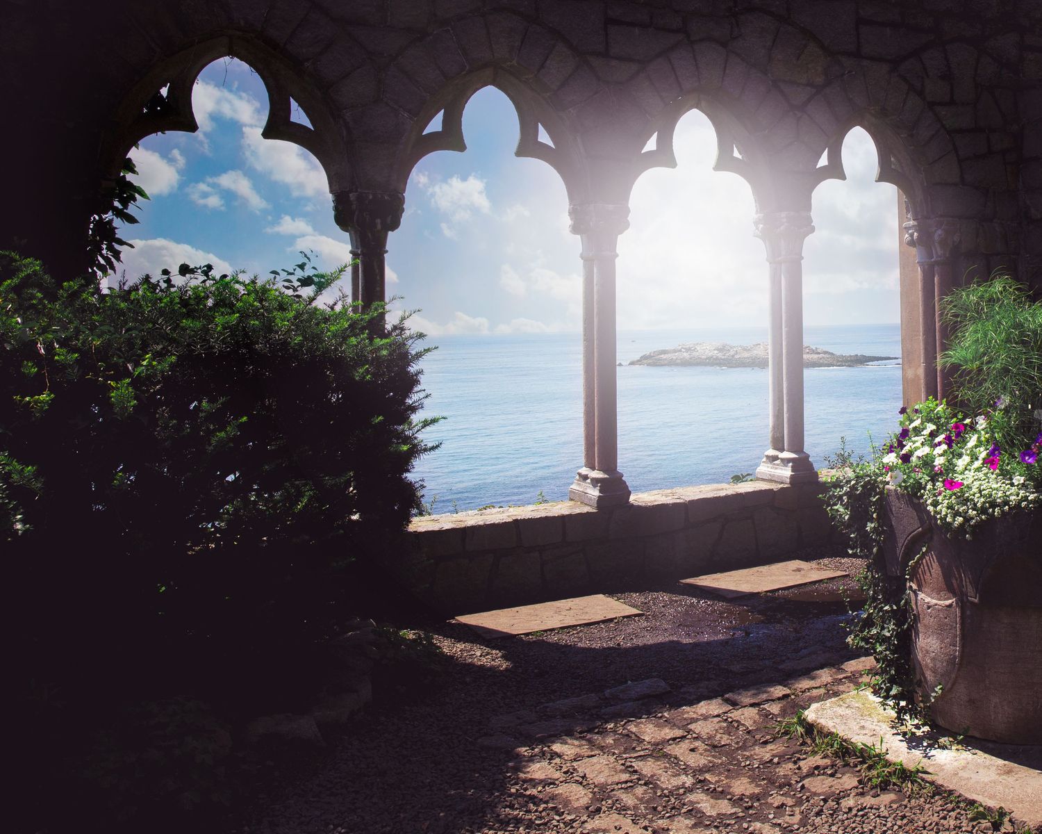 Mediterranean coastal views through stone archways at a scenic overlook with blue sea and sky in the background.