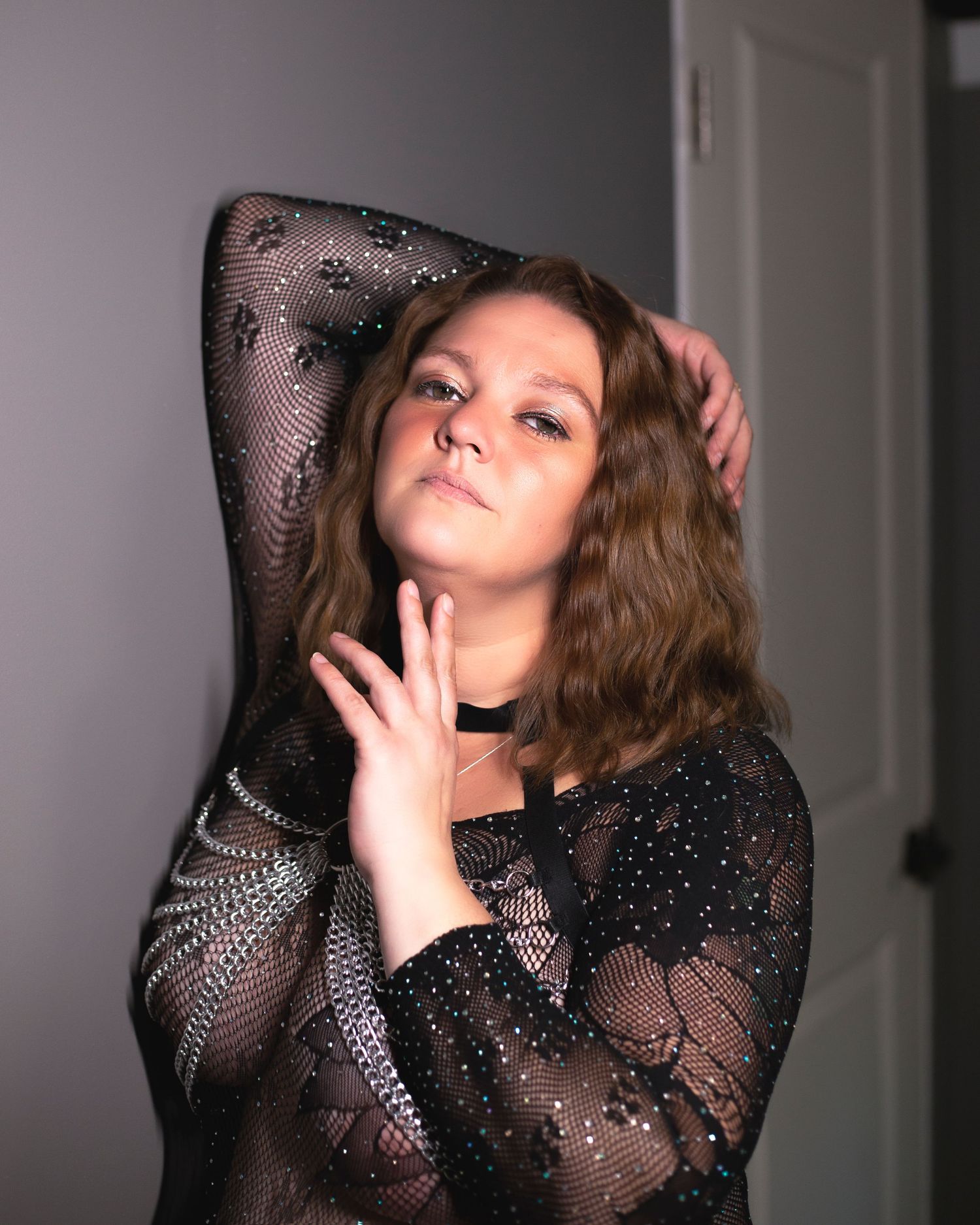 Model in black lace long-sleeve dress poses elegantly against grey backdrop in artistic portrait series.