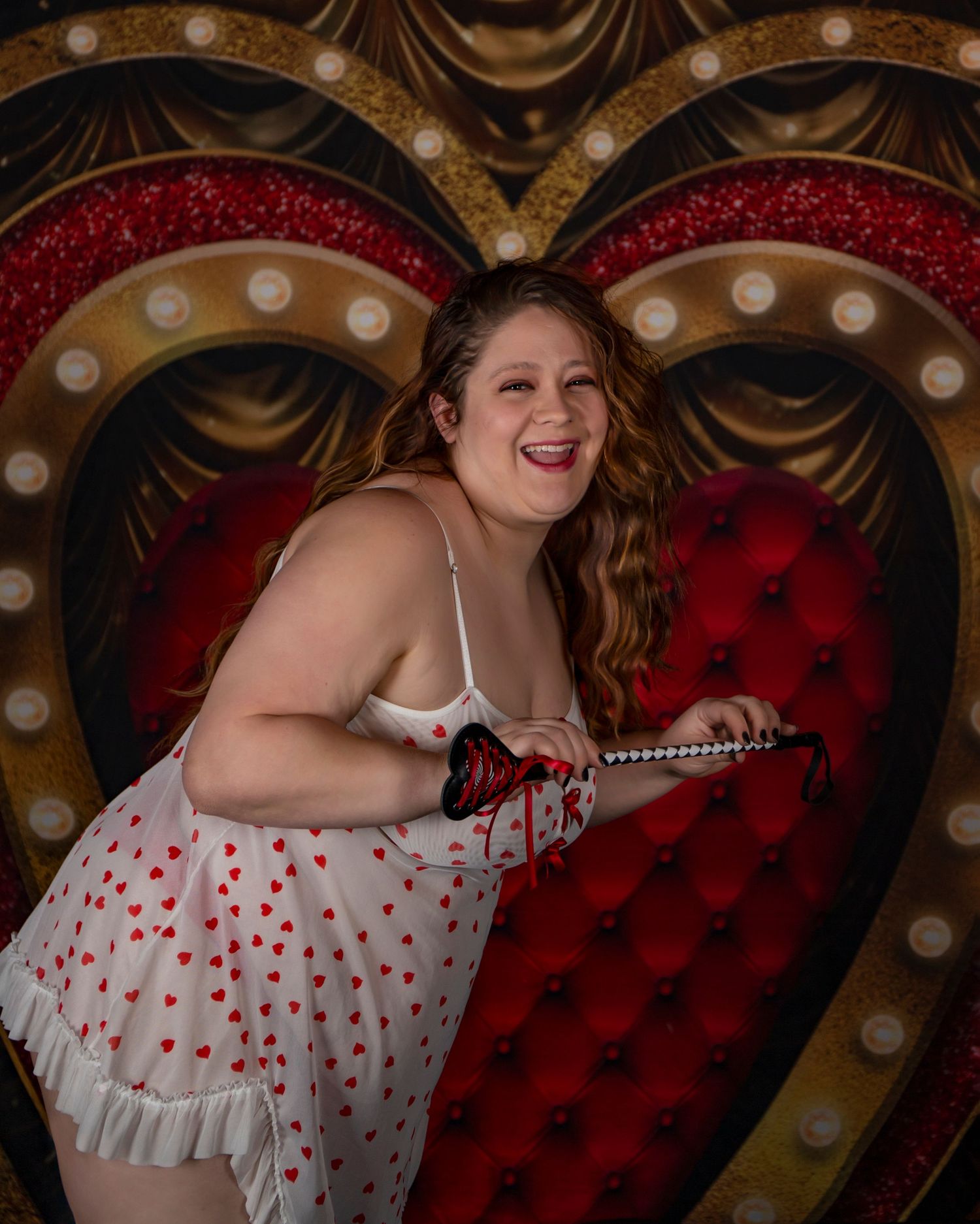 A joyful figure in a white and red polka dot dress poses against a vintage-style heart backdrop with marquee lights.