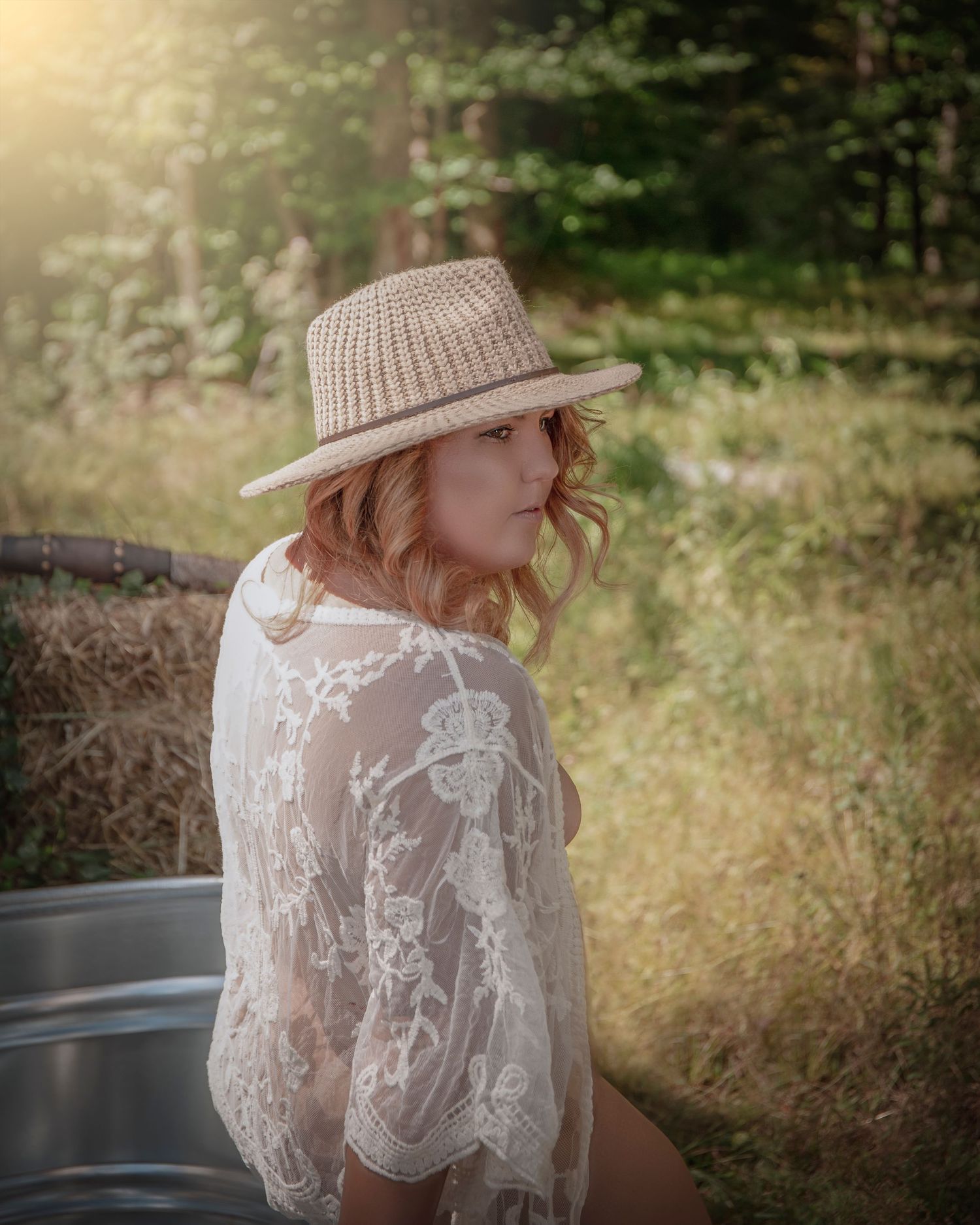 Woman in white lace dress and sun hat poses outdoors in natural sunlit setting.