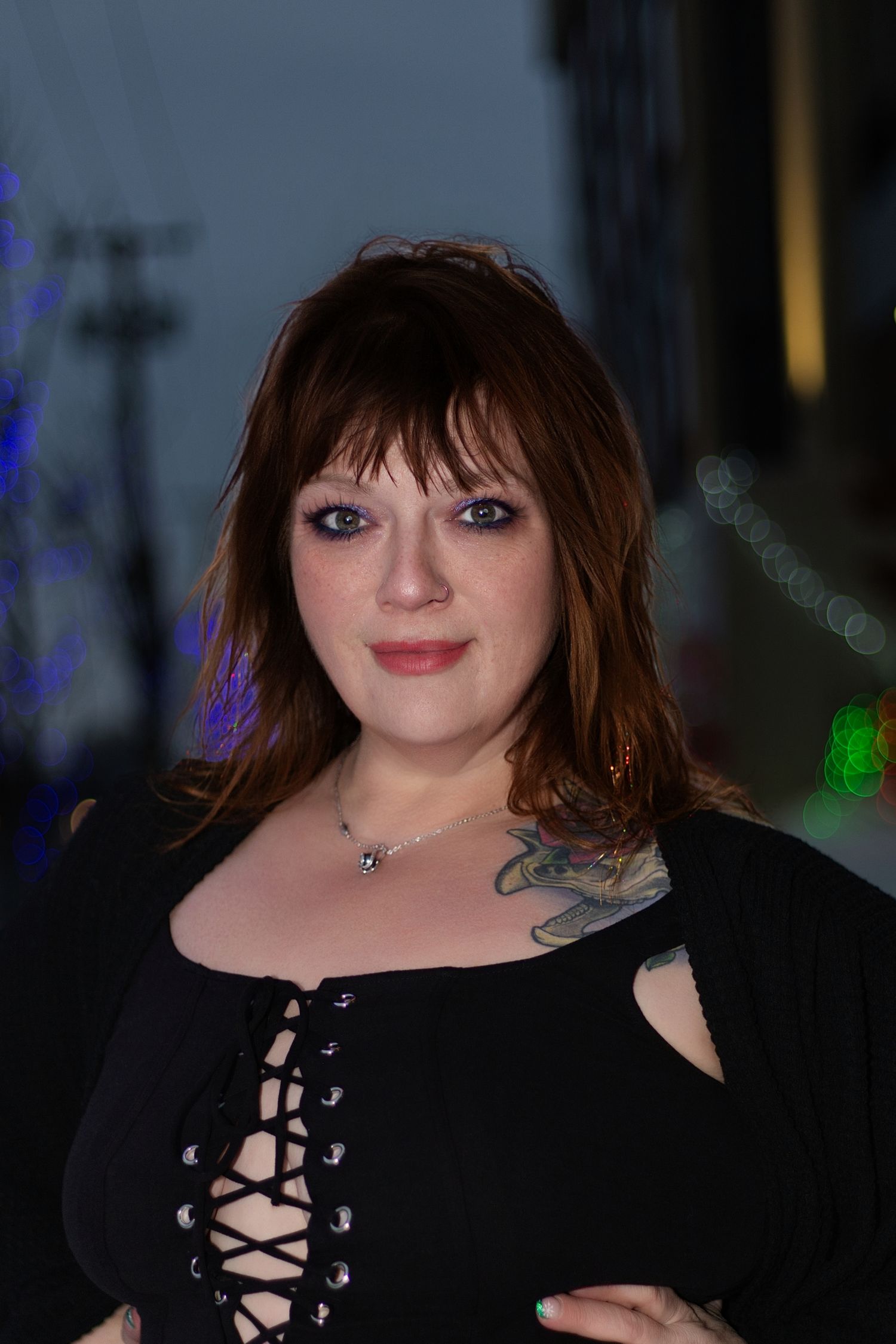 Woman in black lace-up top poses in dramatic lighting with dark background.