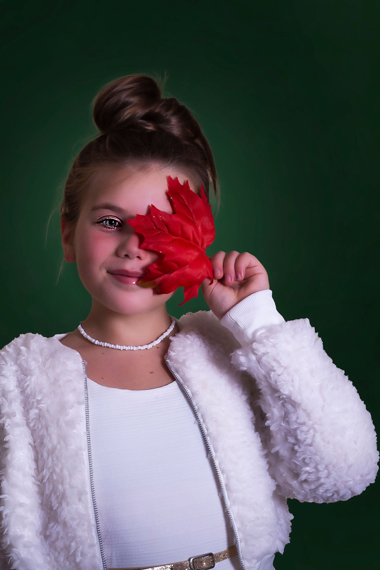 A person in a white fuzzy sweater holds a bright red flower against a dark green background.
