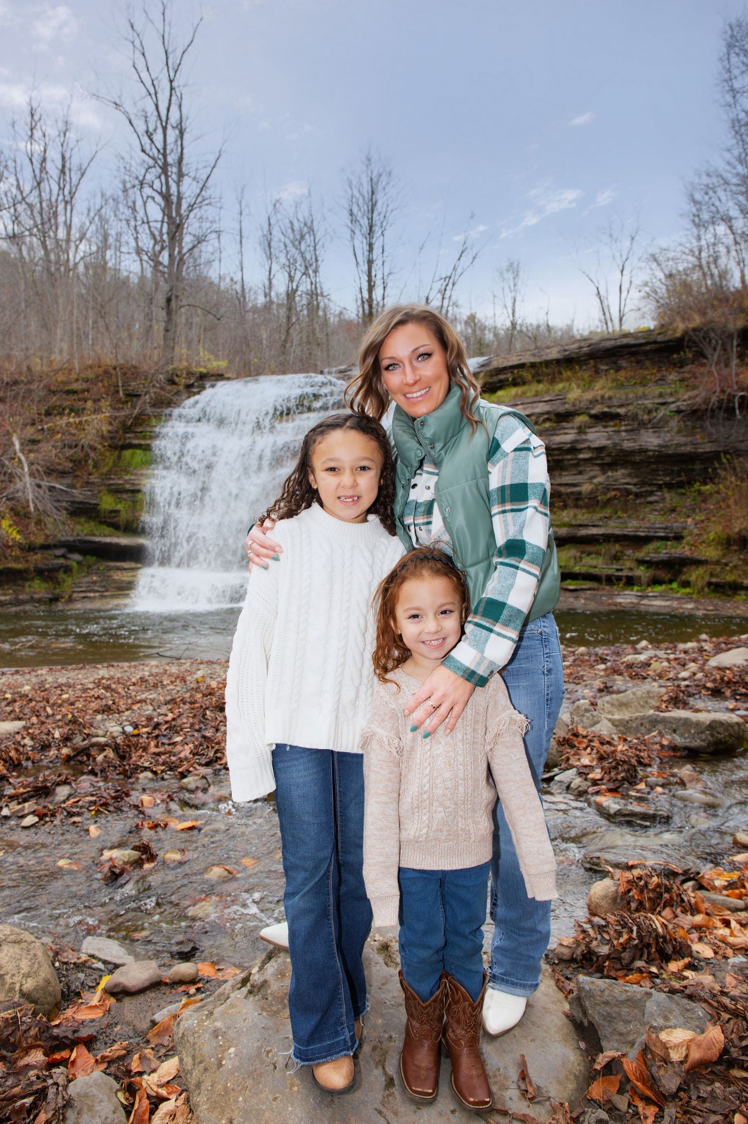 A scenic waterfall forms the backdrop for a family photo on fallen autumn leaves.