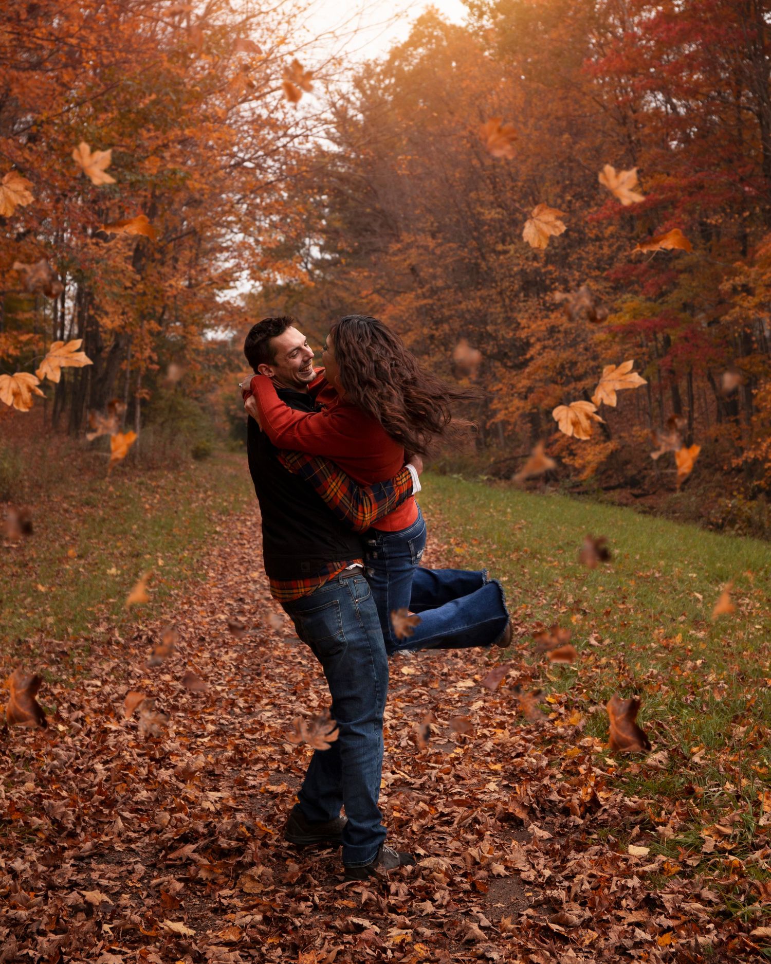Person playing in a pile of autumn leaves on a crisp fall day with orange foliage in the background.