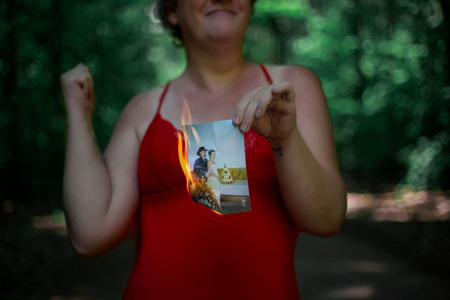A runner in a red tank top holds up a race medal in a wooded outdoor setting after completing an event.