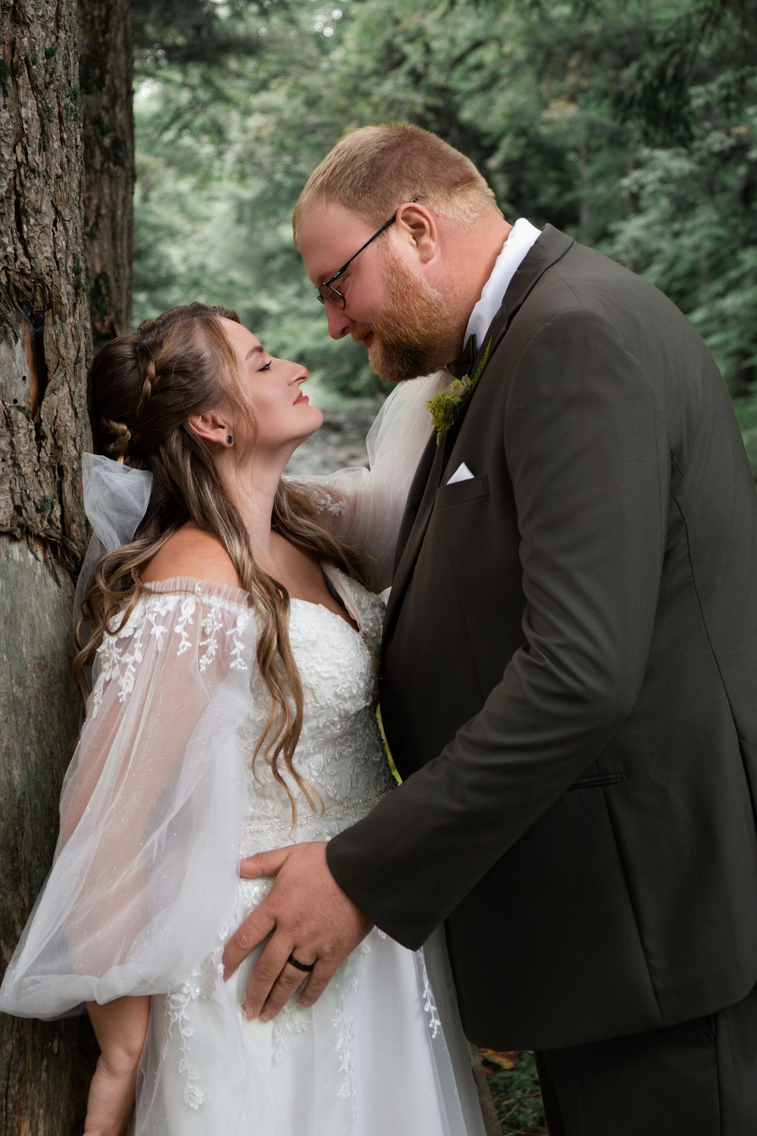 Romantic wedding couple embrace among pine trees in forest setting.
