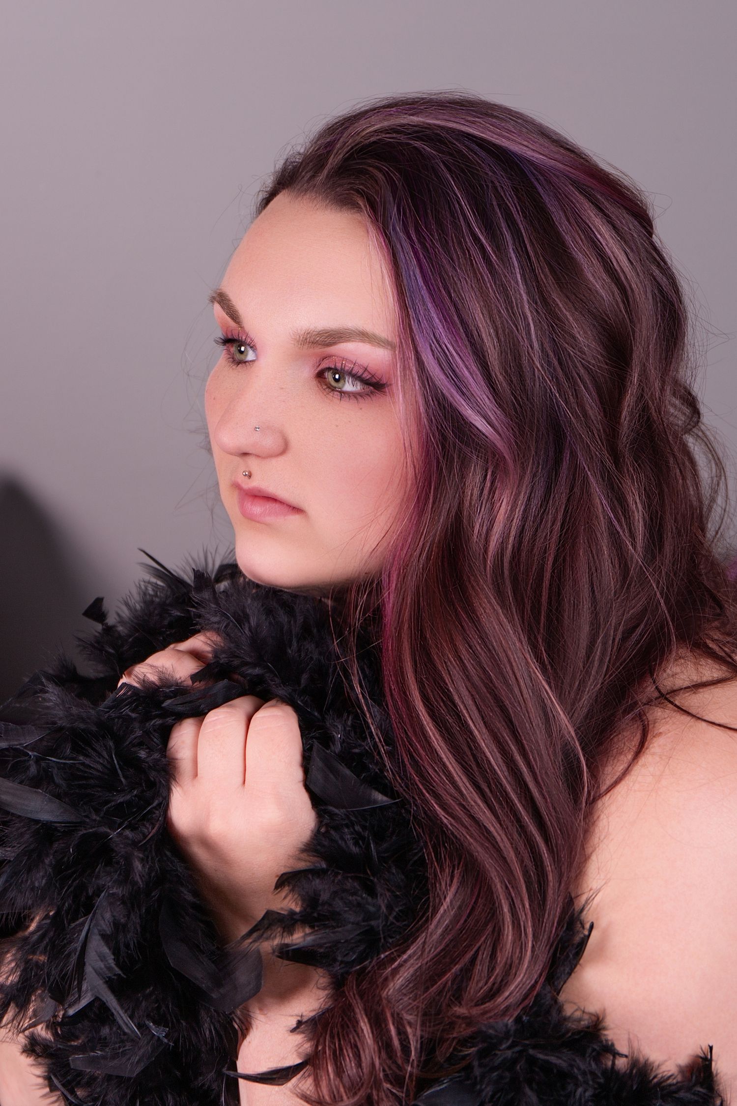 A series of artistic portraits featuring wavy burgundy hair and black feather accessories against a dark background.