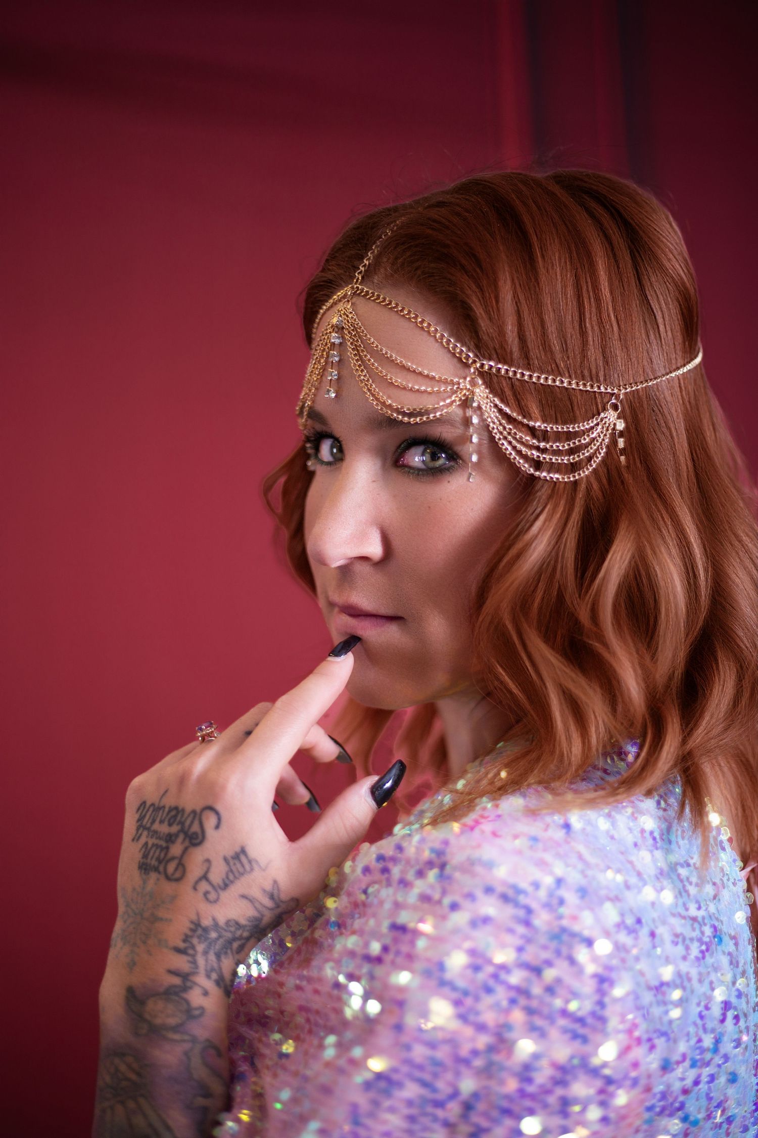 Sparkly sequin dress and delicate chain headpiece complement the red backdrop in this glamorous portrait.