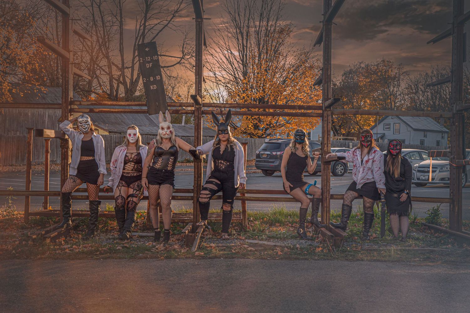 A group of people gather at a skatepark during sunset with warm golden lighting and autumn trees in the background.