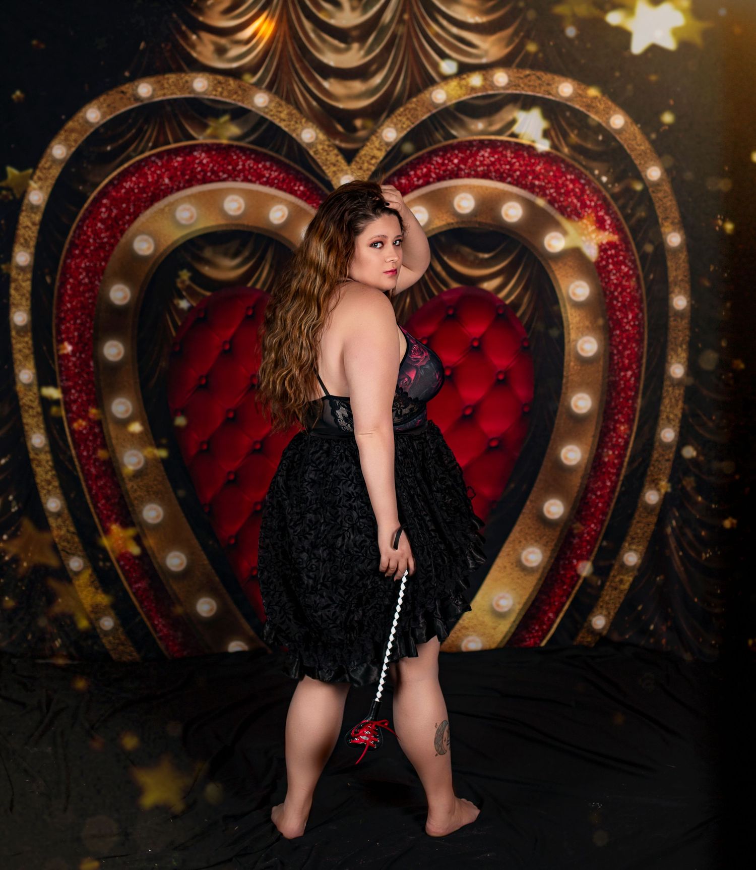 Plus size model in black dress poses in front of illuminated vintage heart backdrop.