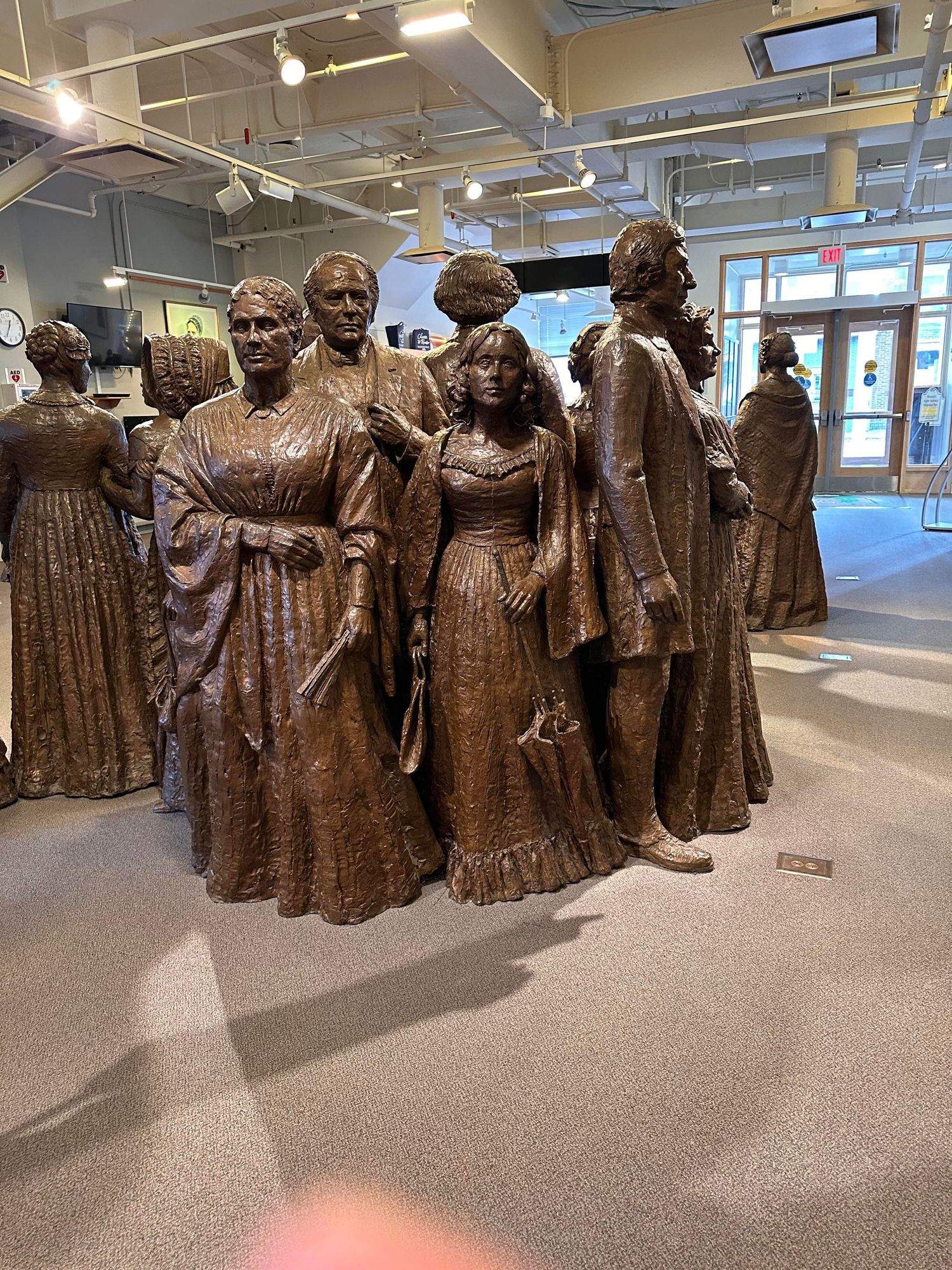 Bronze sculpture installation depicting a group of historical figures standing together in an indoor gallery space.
