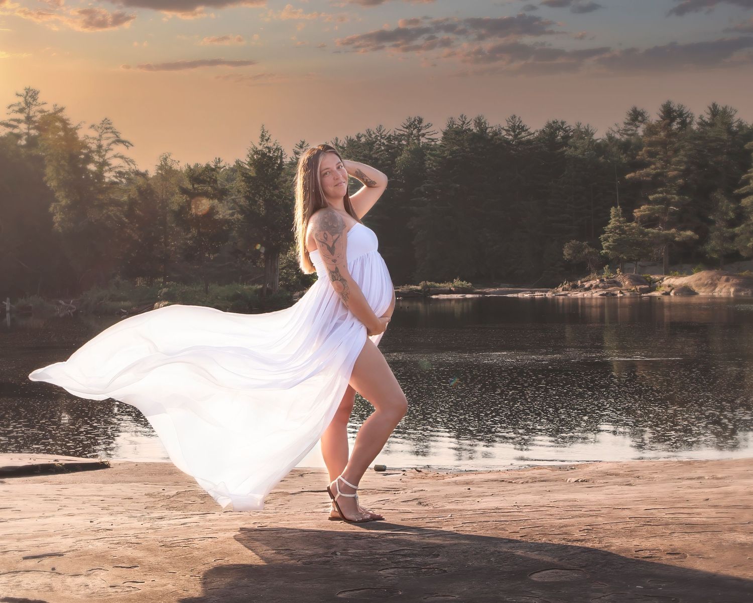 A flowing white dress catches the wind during a sunset photoshoot by a lake.