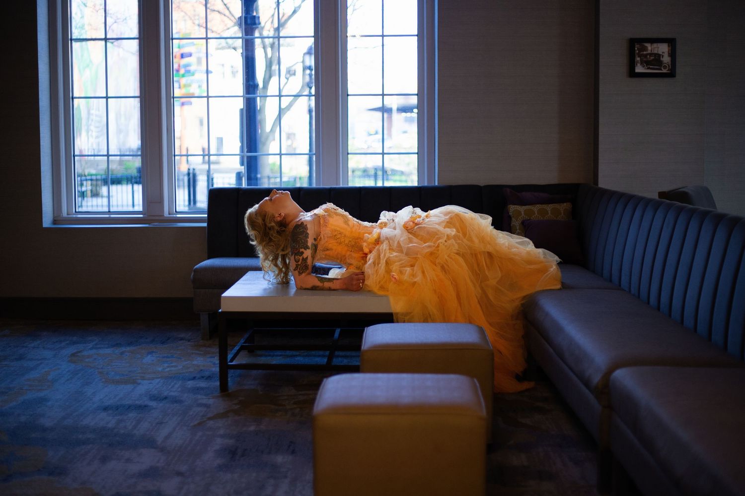 A yellow ball gown drapes across a blue sofa near a bright window, creating a dreamy indoor scene.