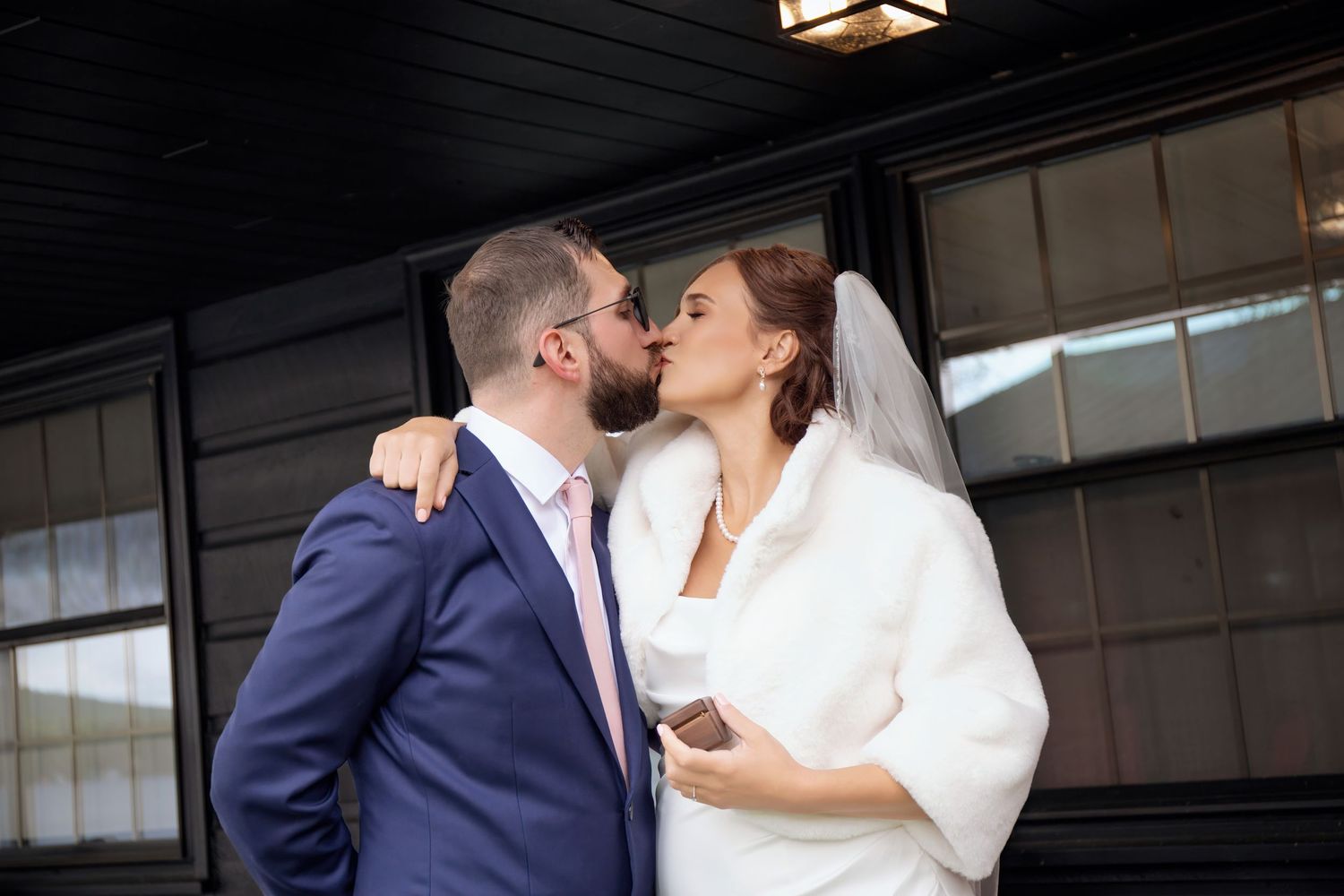 A couple shares a romantic kiss on their wedding day, with the bride in white and groom in navy blue.