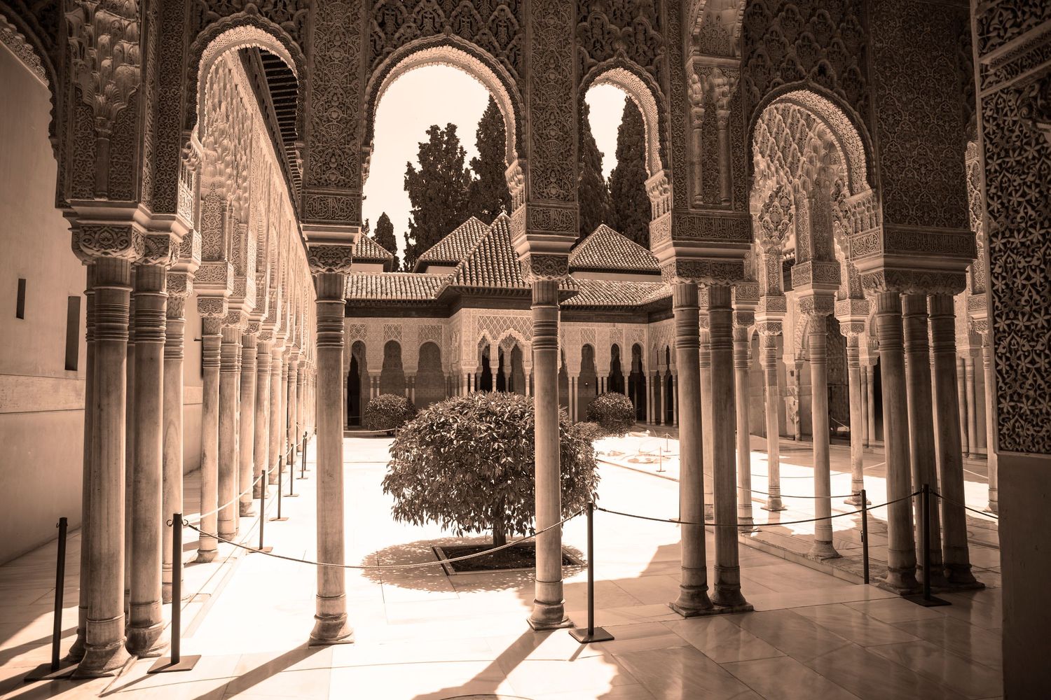 Sunlight streams through ornate Moorish arches in the historic Alhambra palace courtyard in Granada, Spain.