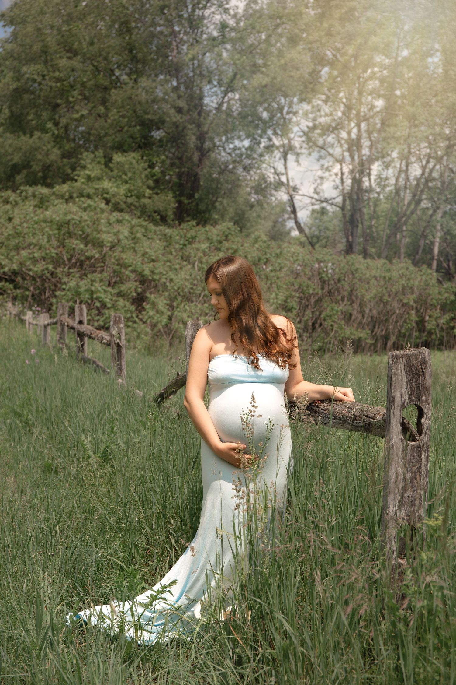 A person in a light blue dress poses gracefully in a field of tall grass during golden hour.