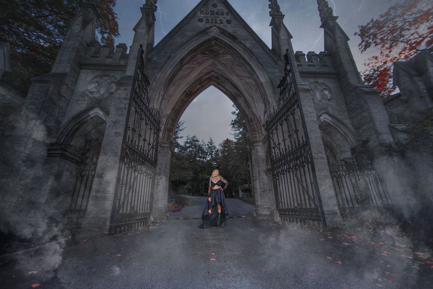 Misty gothic archway entrance to cemetery with figure standing in atmospheric fog at dusk.