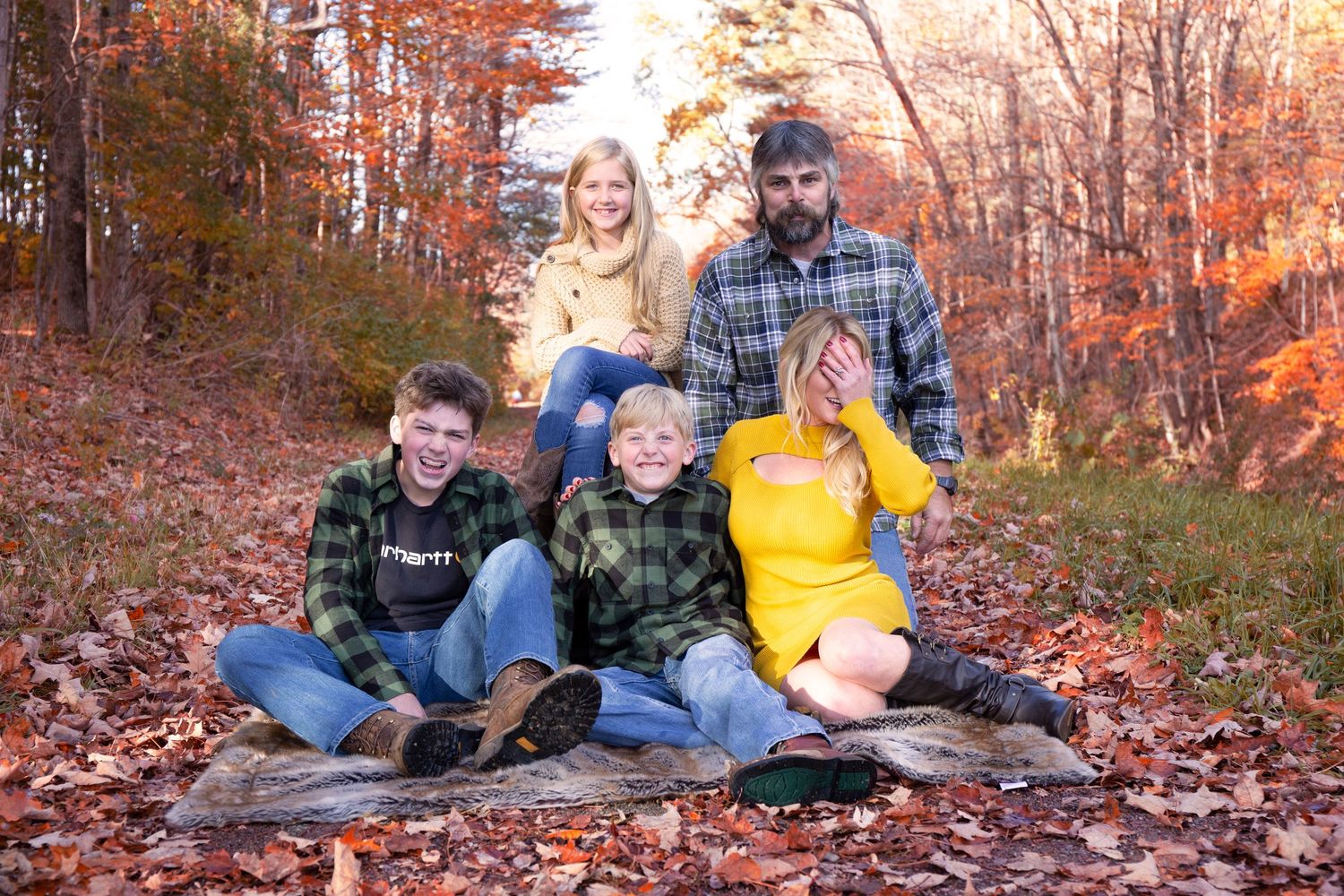Family autumn photoshoot with fallen leaves in a wooded setting during sunset.