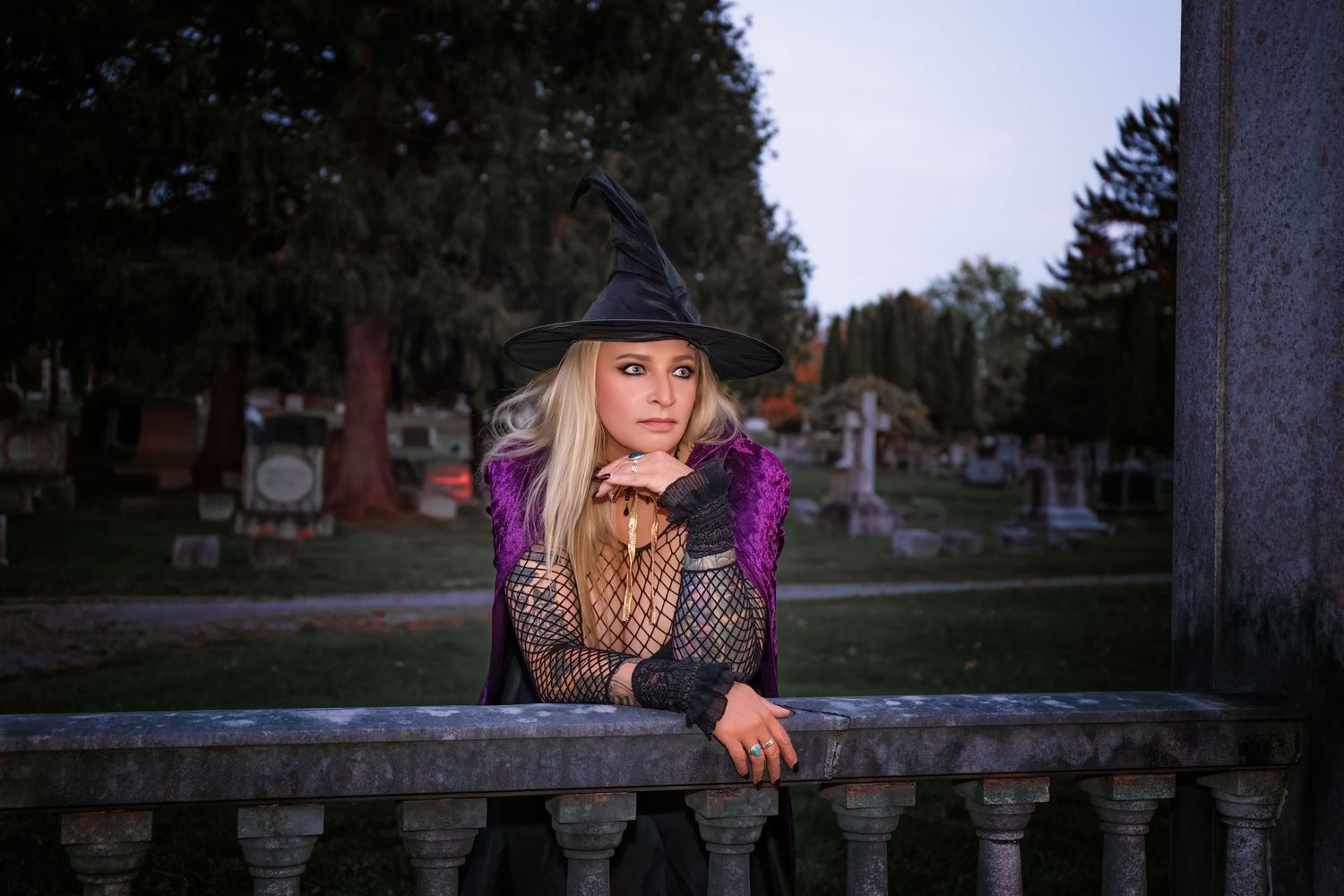 A person wearing a black hat peers over a wooden fence at sunset.